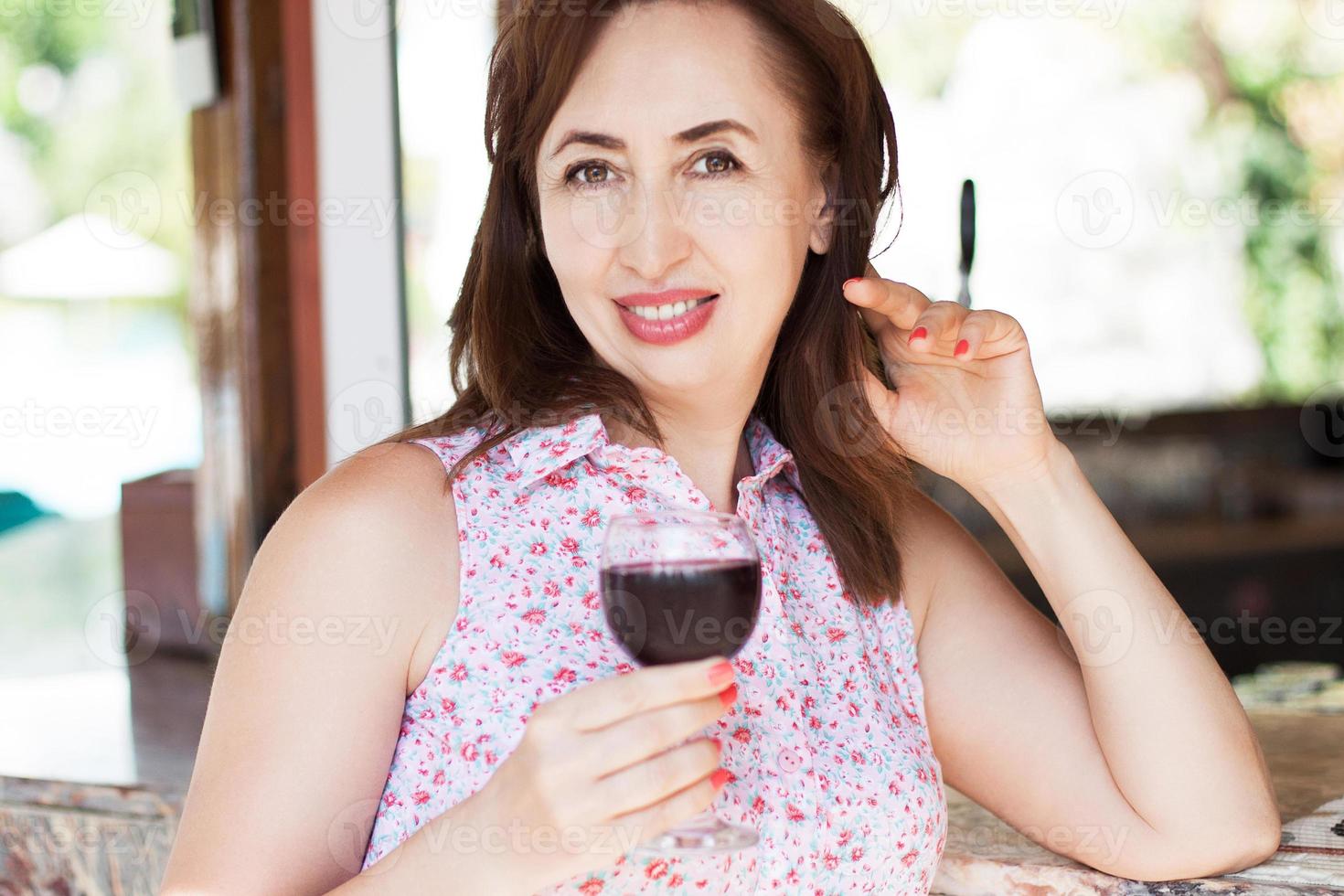 hermosa mujer feliz de mediana edad sostiene una copa de vino en el resort en sus vacaciones, concepto de vacaciones de verano. foto