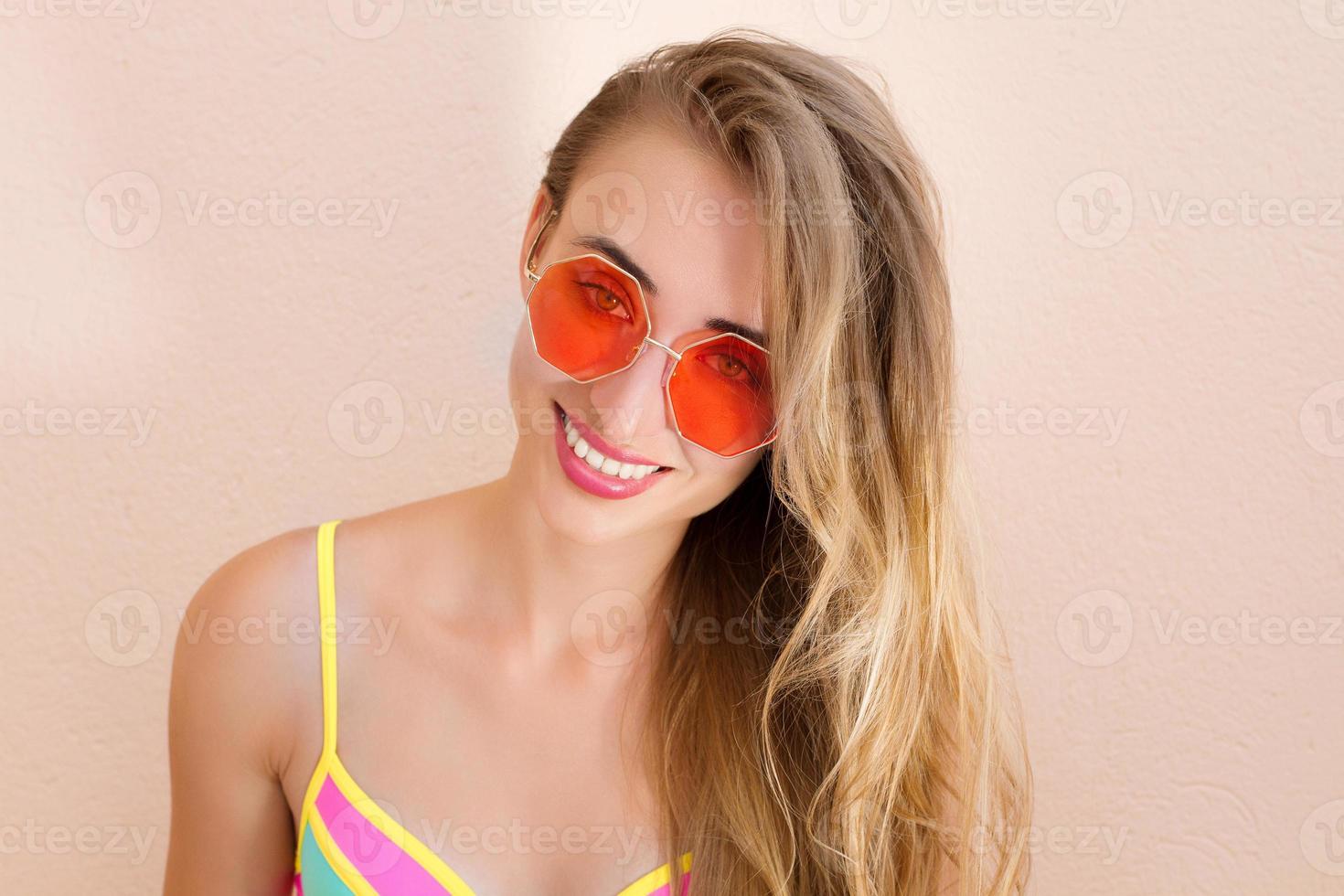 cerca de una chica feliz con gafas de sol rosas aisladas. vacaciones de verano y fin de semana divertido. concepto de verano. mujer joven sonriente en traje de baño de moda. enfoque selectivo. traje de playa de verano. copie el espacio foto