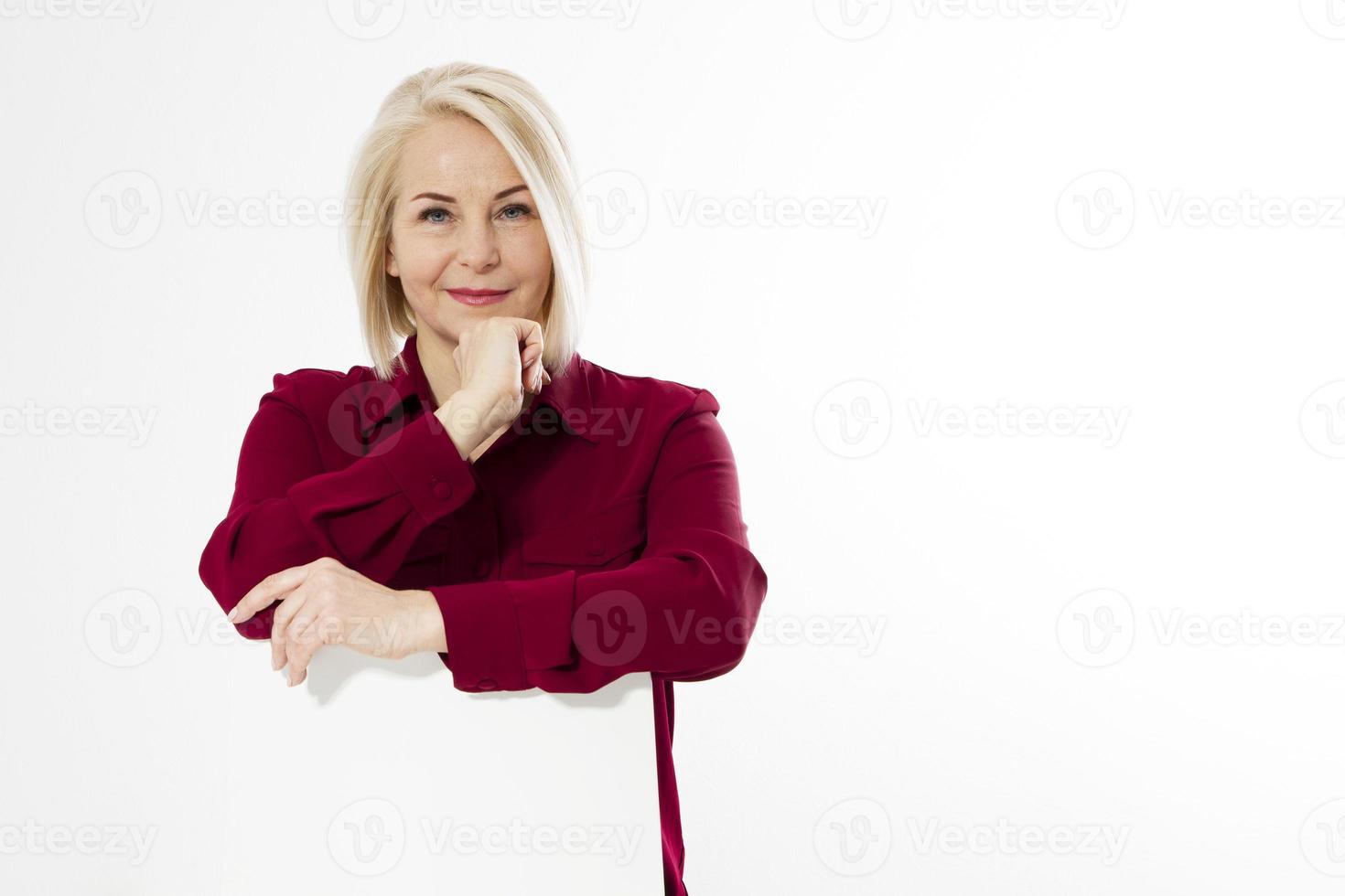 retrato de una alegre y sonriente mujer rubia de mediana edad sentada en una silla aislada en blanco foto