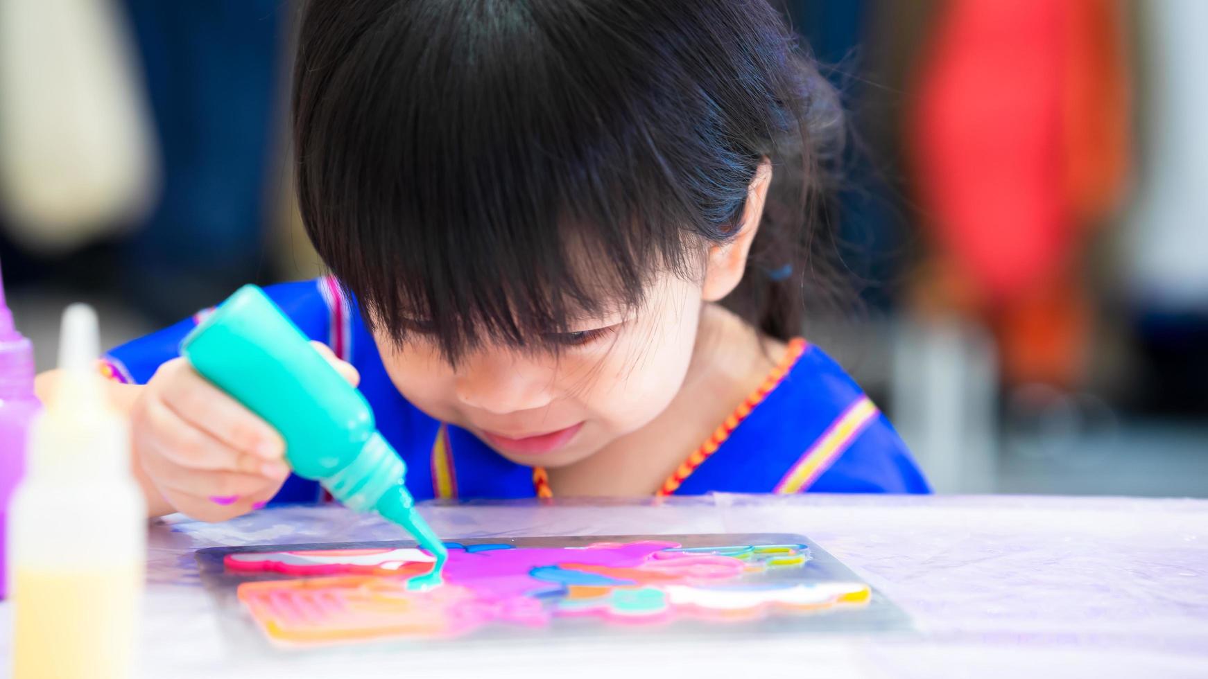 Cute kid girl is sitting blue watercolor paint onto stainless steel plate to create beautiful pattern. Happy child with artwork. photo