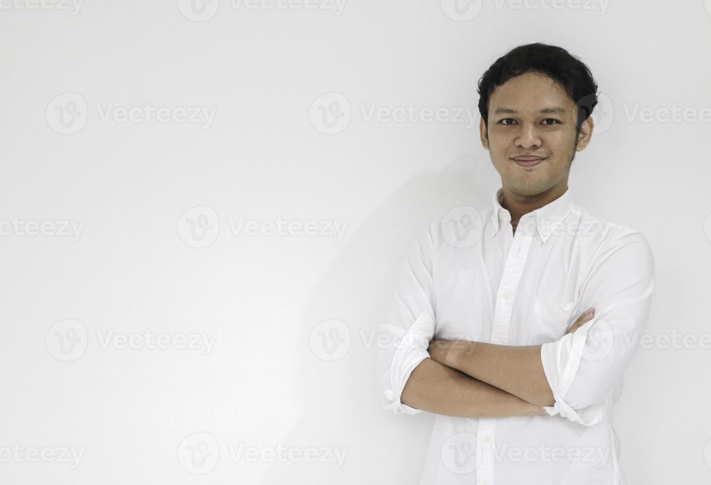 Young Asian man wearing white shirt is holding hands crossed with happy smile and confidence. Successful Indonesian man on gray background. photo