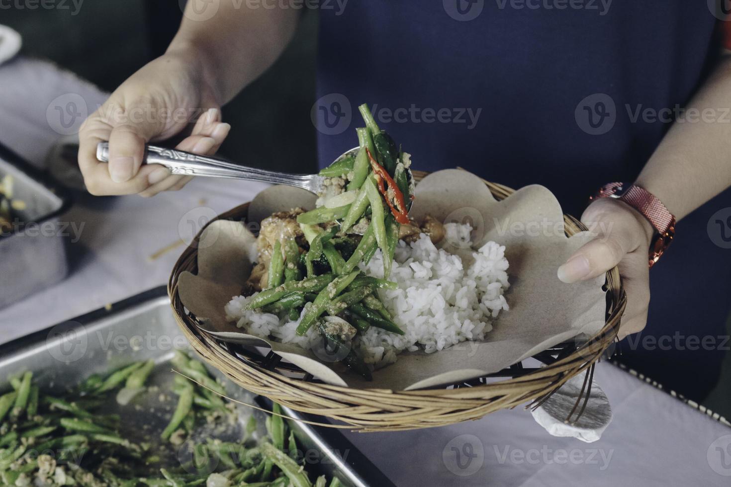 la mano de la persona pone verduras blancas de la sartén de acero al plato de papel de madera durante el almuerzo en el restaurante foto