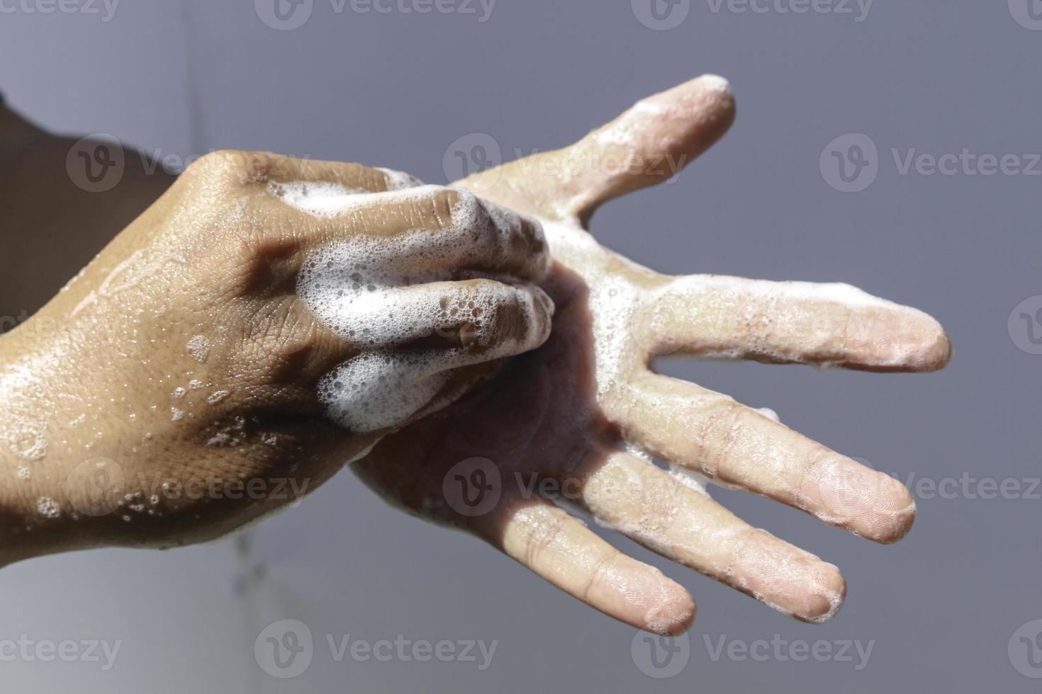 el hombre usa jabón y se lava las manos con fondo gris bajo la luz del sol. detalle de la mano del concepto de higiene foto