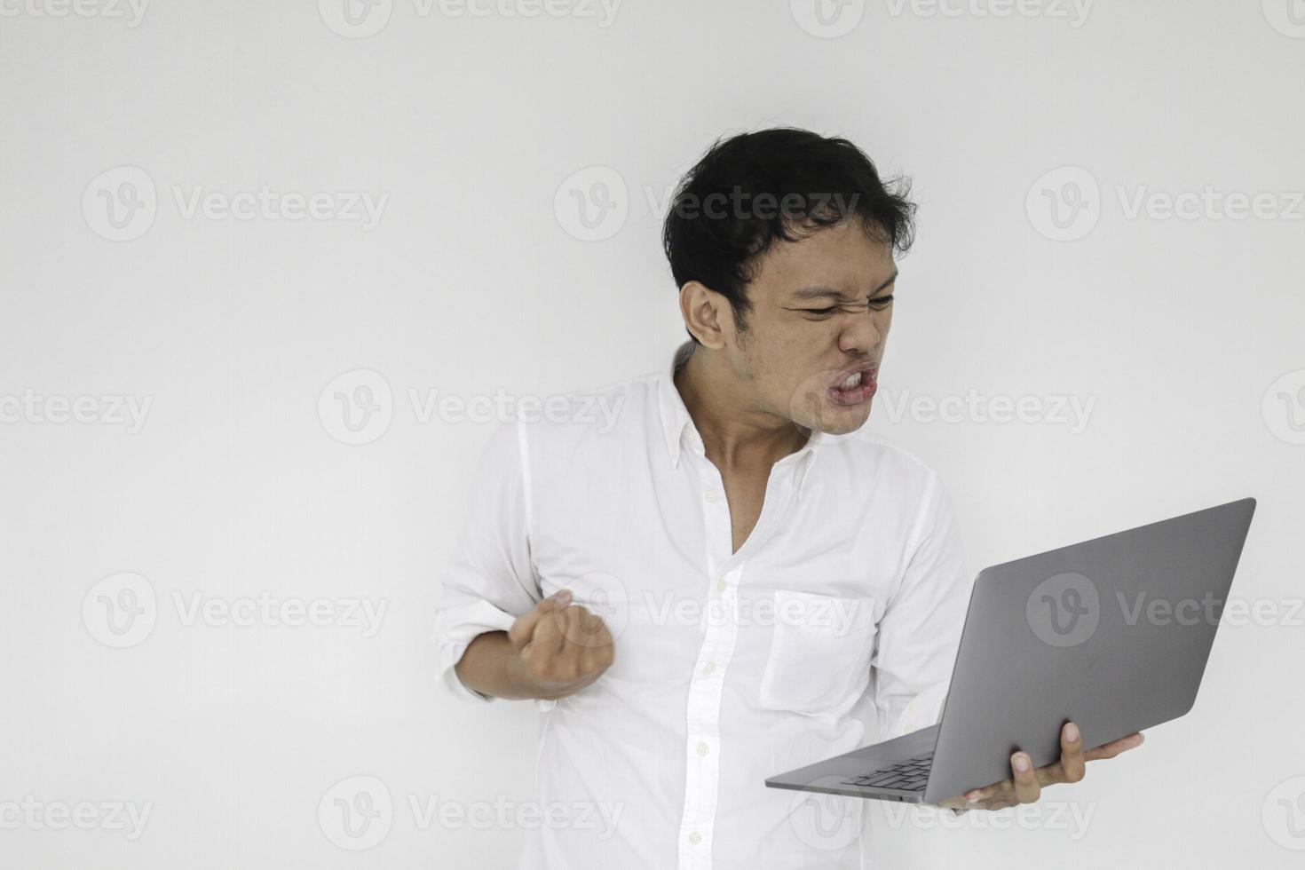Young Asian man is Angry and hate with laptop. Indonesia Man wear white shirt Isolated grey background. photo