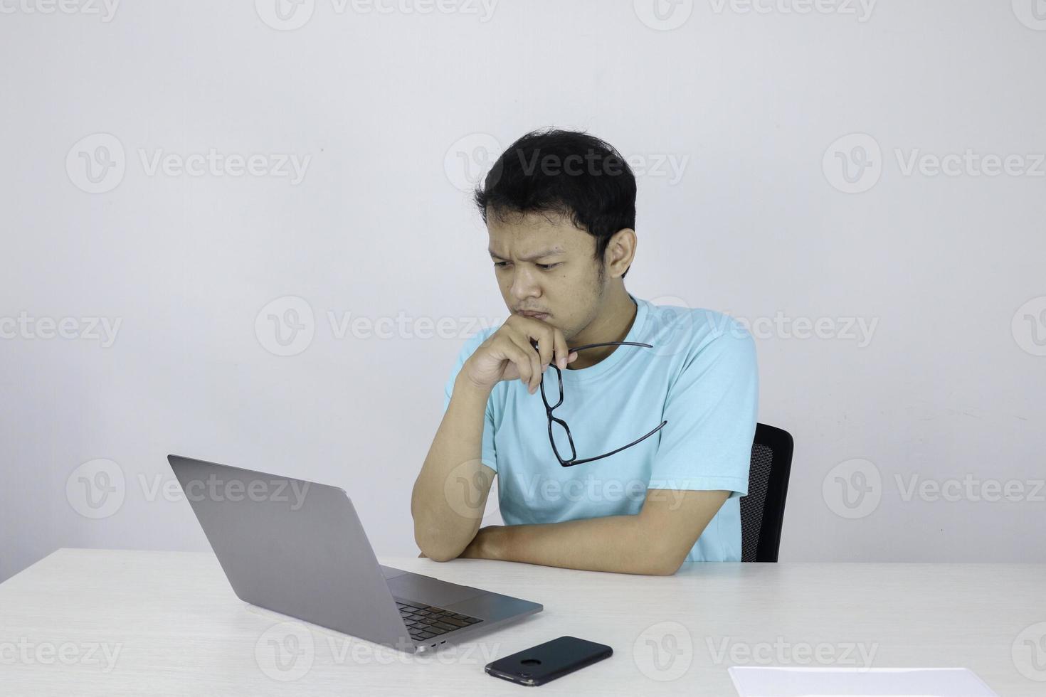 Young Asian Man is serious and focus when working on a laptop on the table. Indonesian man wearing blue shirt. photo