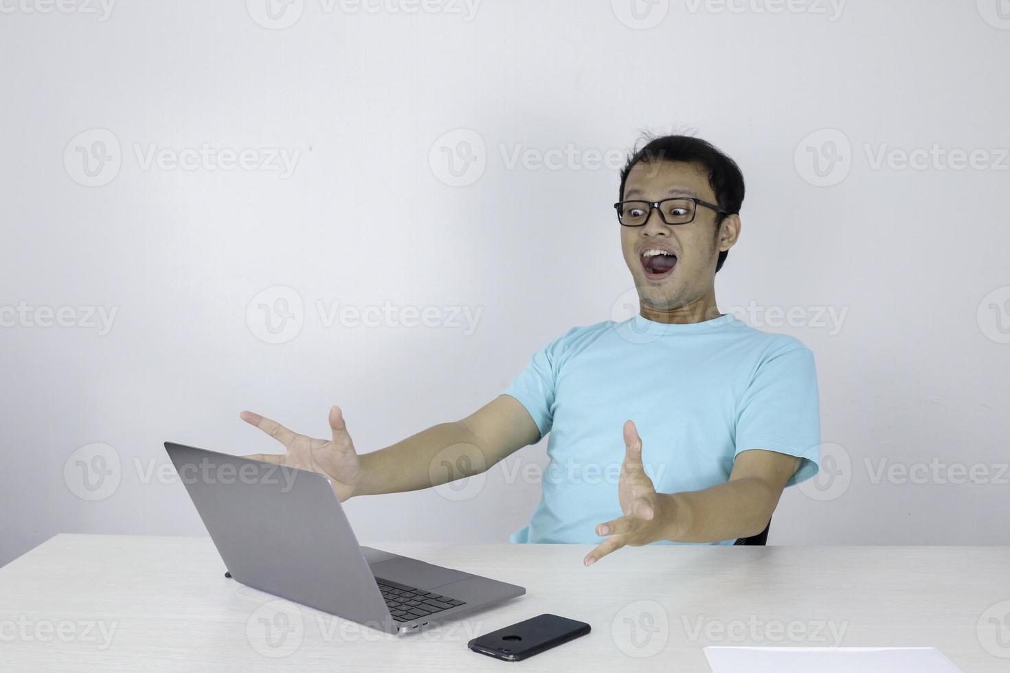Wow face of Young Asian man shocked what he see in the laptop when working isolated grey background wearing blue shirt. photo