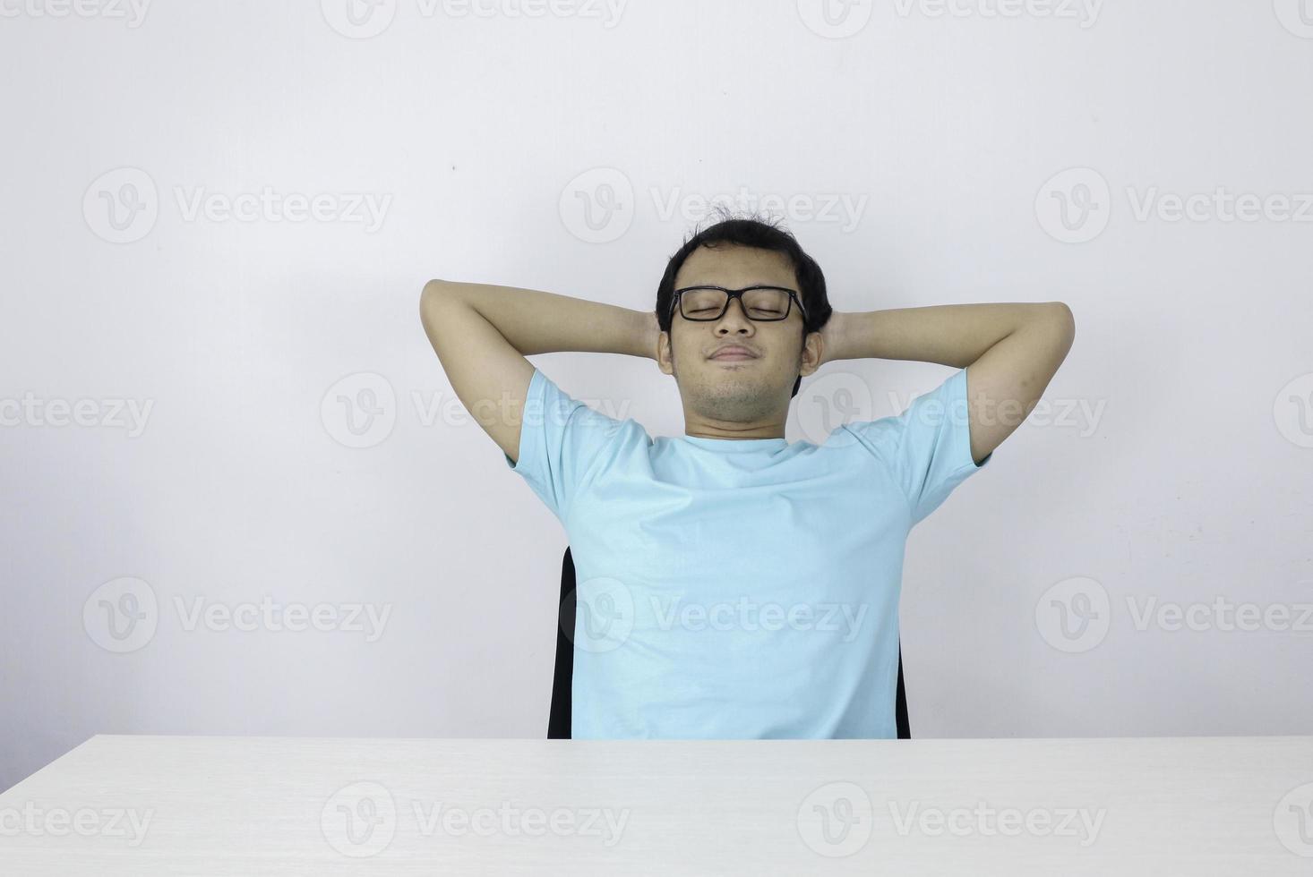 un joven asiático tranquilo y sonriente que se relaja en una cómoda silla de oficina con las manos detrás de la cabeza, un hombre feliz descansando en la oficina satisfecho después del trabajo hecho, disfrutando de un descanso con los ojos cerrados, tranquilidad, sin estrés foto