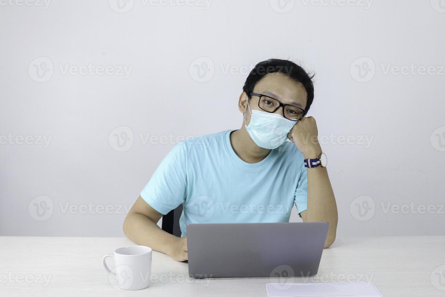 Young Asian man wearing medical mask is feeling unhealthy, tired, and confuse with work in laptop. photo