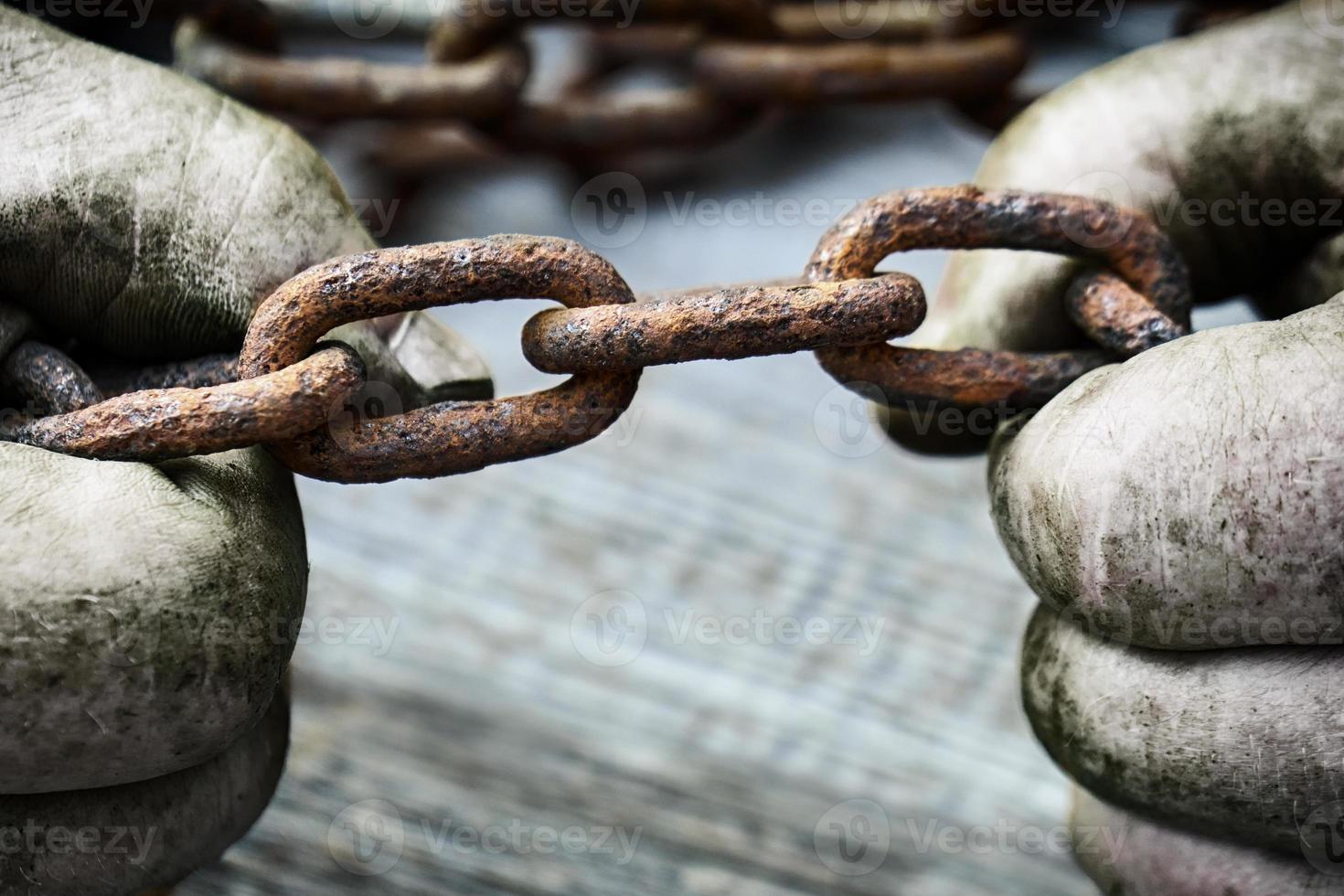 Powerful male hands trying to tear an old rusty chain photo