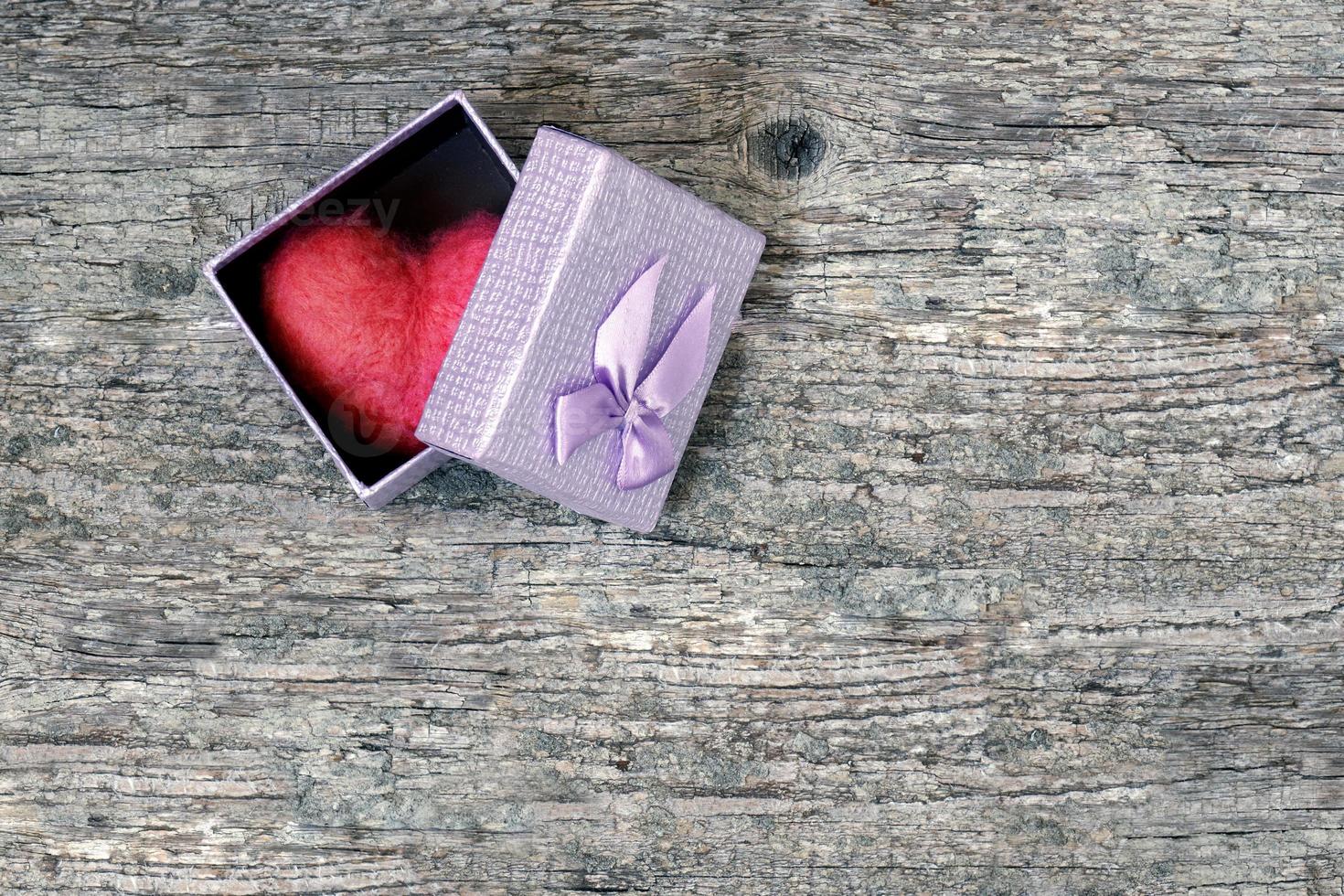 Red wool toy heart lying in a open gift box on a wooden table. Heart as a gift. photo