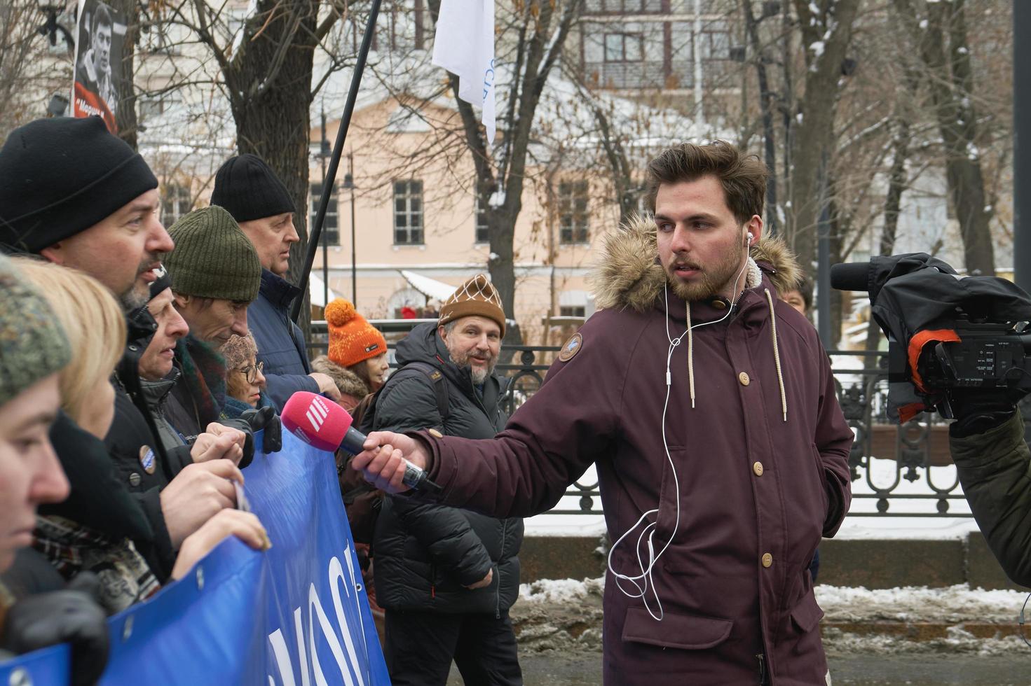 Moscow, Russia - February 24, 2019. Nemtsov memorial march. Reporter of the Russian TV Rain channel Aleksei Korostelev interviewing demonstrators carrying a political banner photo