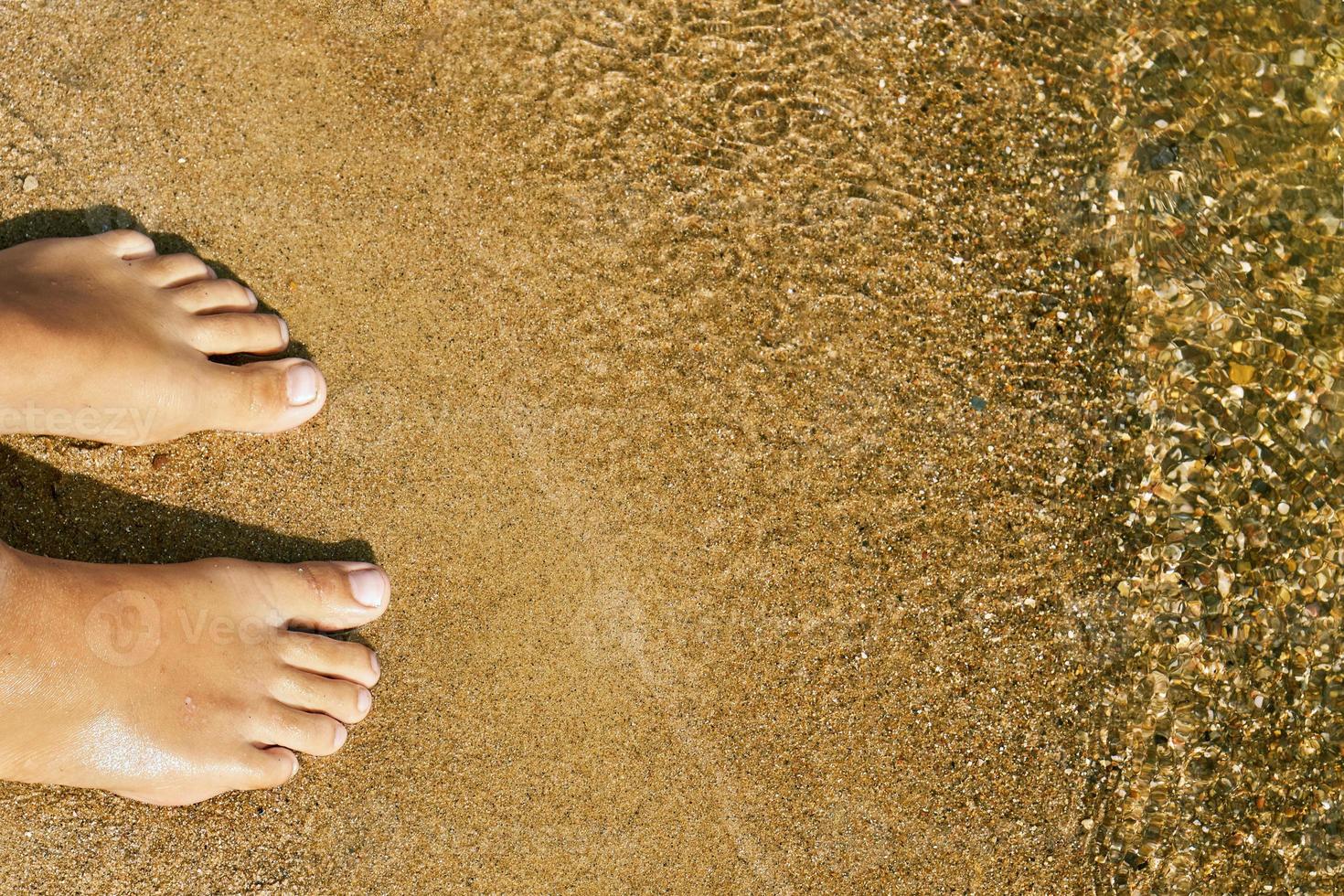 Teen girl's bare feet standing on the sand of a lake beach near the water photo