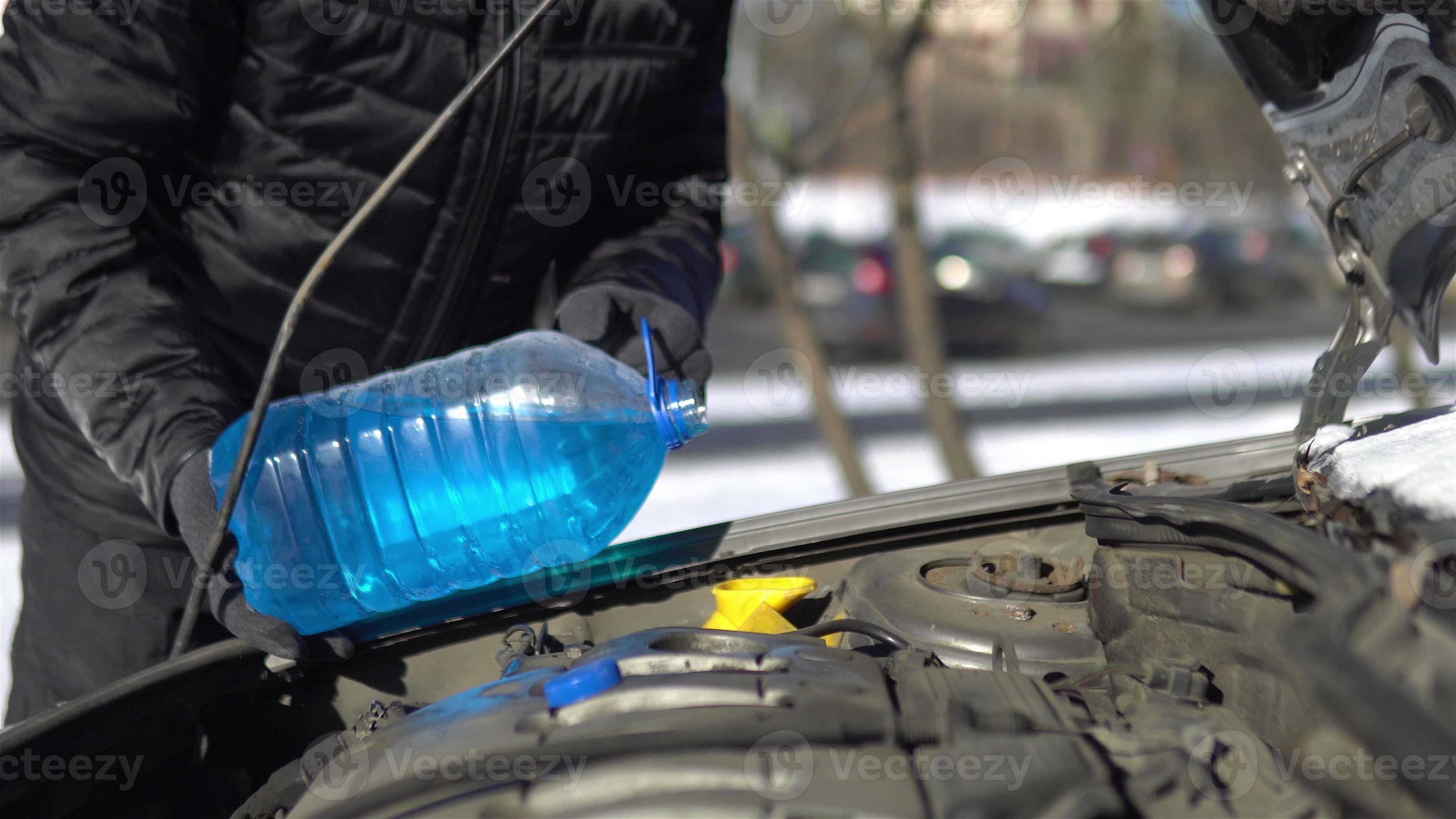Man pouring an antifreeze liquid into a windshield washer tank of a car
