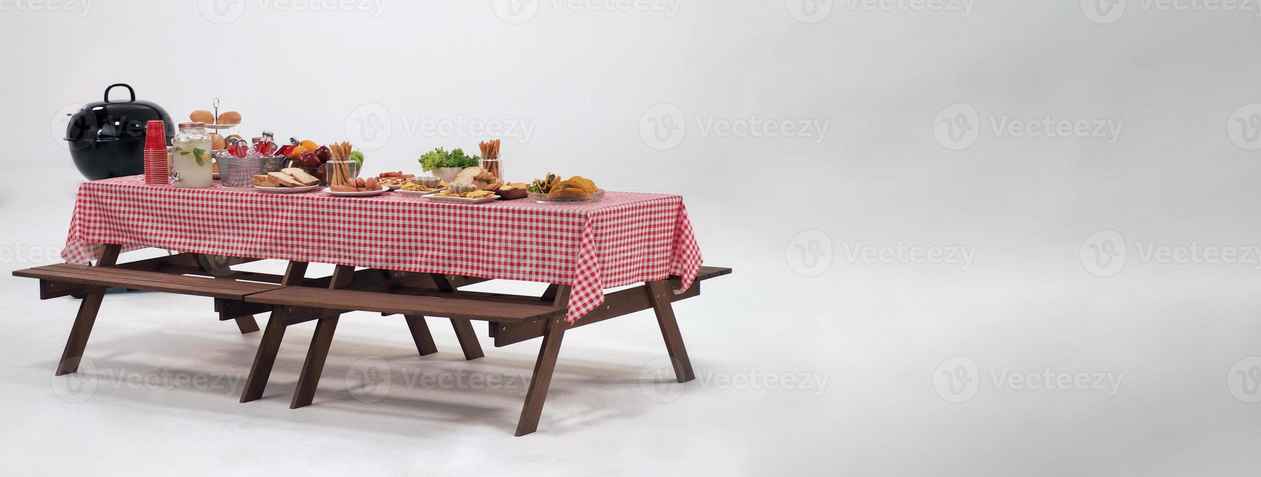 Picnic table and red checkered tablecloth with food and drink for outdoor party. Isolated photo