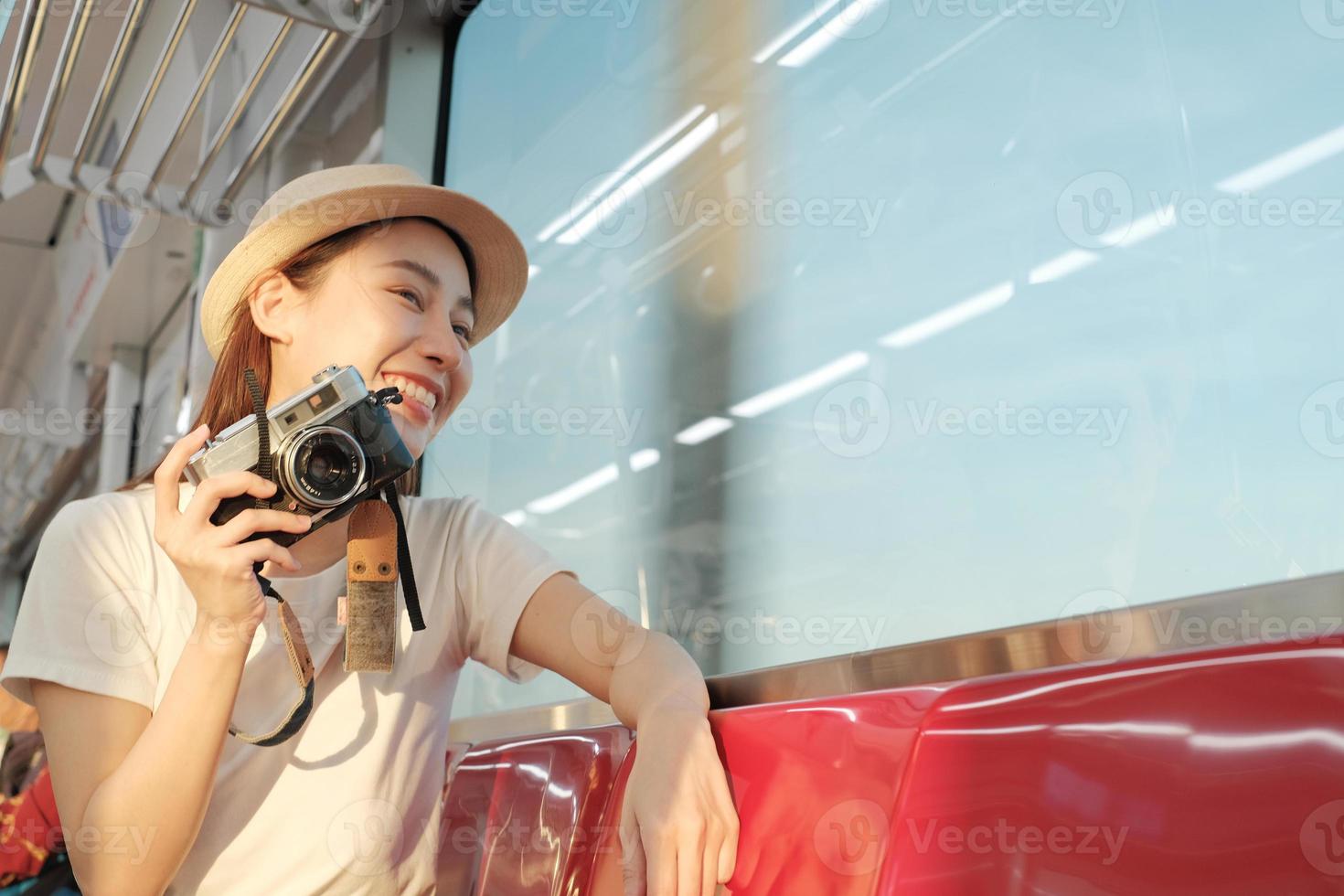 Beautiful Asian female tourist sits in a red seat, traveling by train, taking snapshot photo, transporting in suburb view, enjoy passenger lifestyle by railway, happy journey vacation. photo