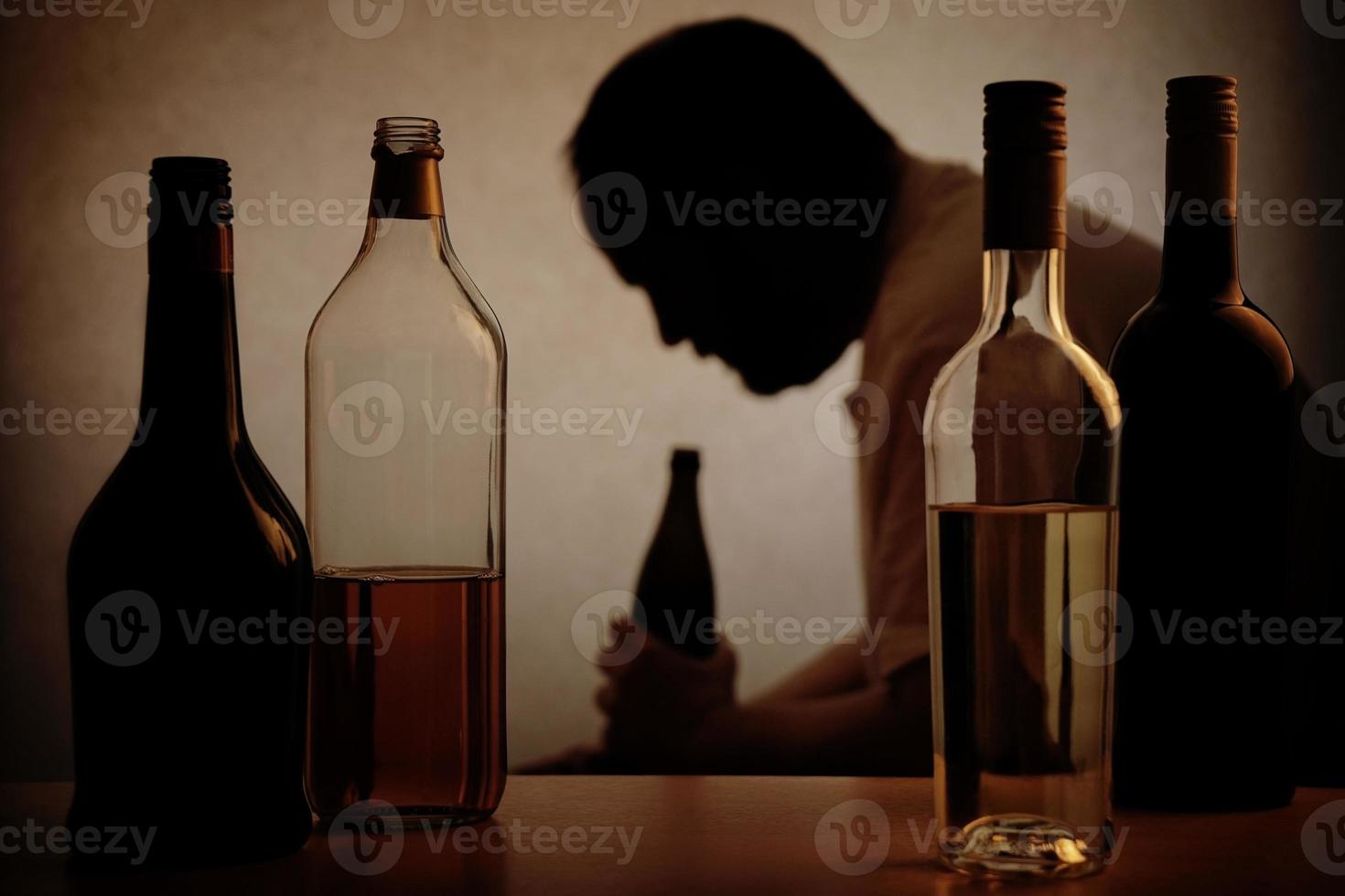 alcoholism - silhouette of man behind aclcohol bottles photo