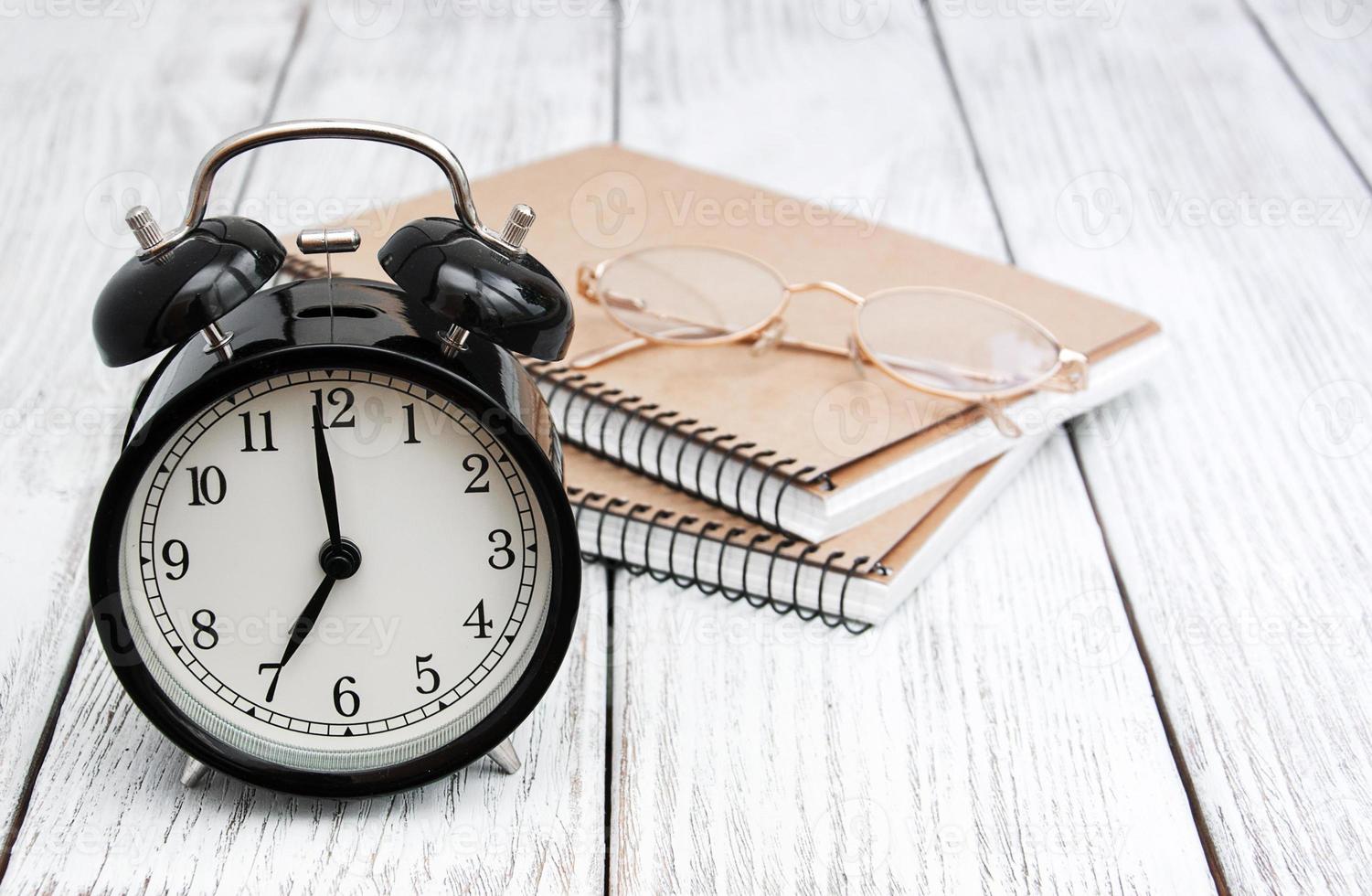 Black alarm clock, notebooks and glasses photo