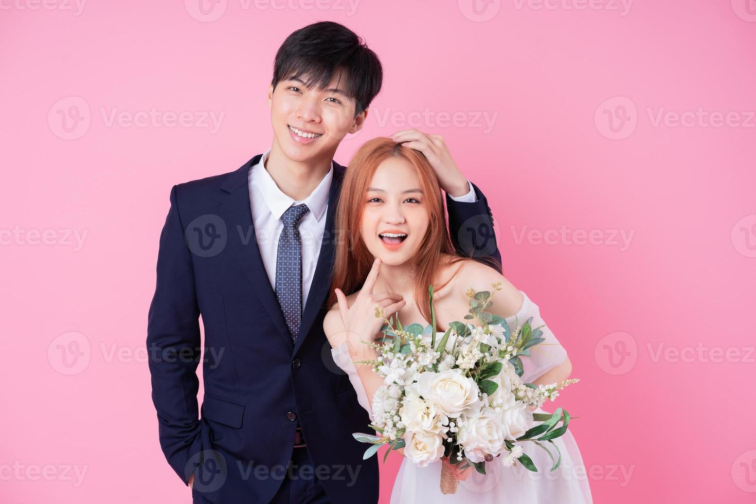 Young Asian bride and groom posing on pink background photo