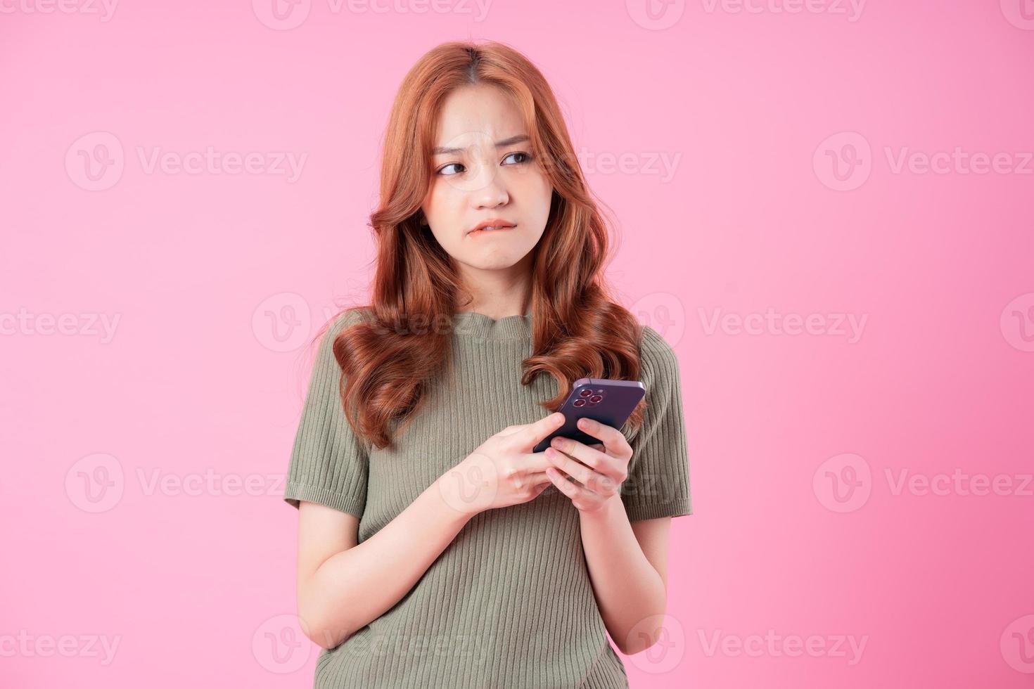 Young Asian woman using smartphone on pink background photo