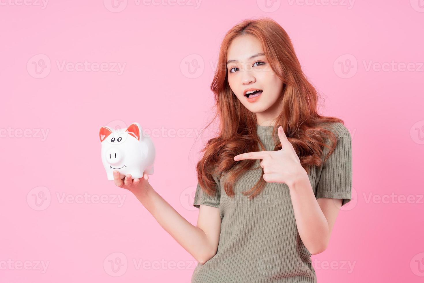 joven asiática sosteniendo una alcancía con fondo rosa foto