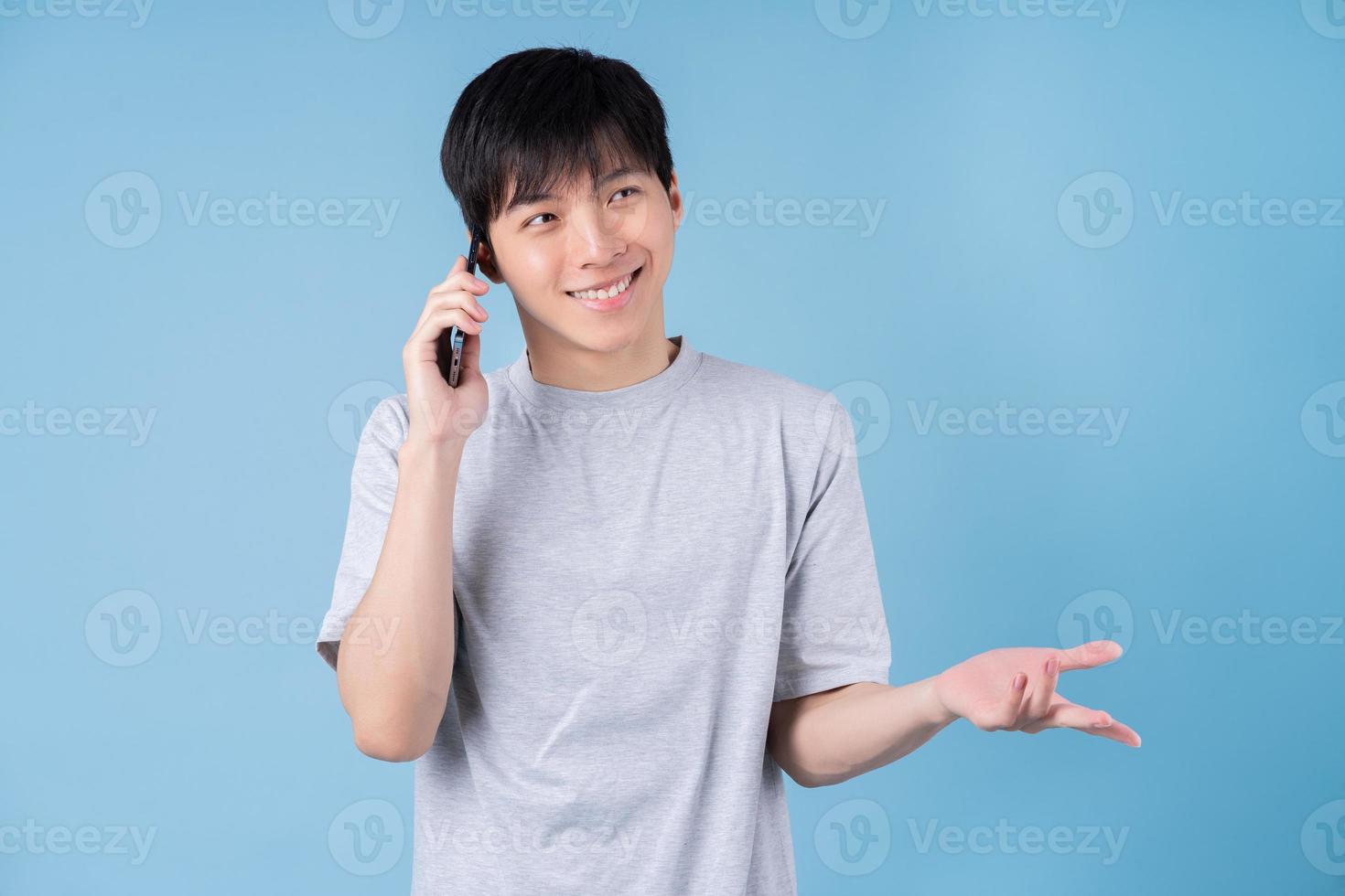 Young Asian man using smartphone on blue background photo