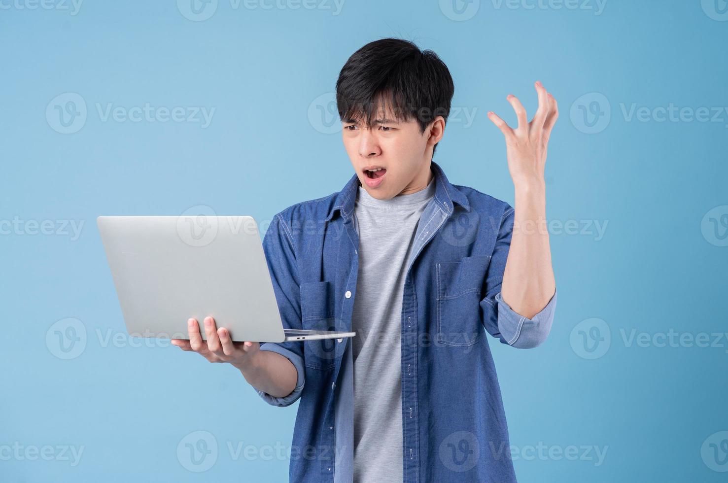 Young Asian man using laptop on blue background photo