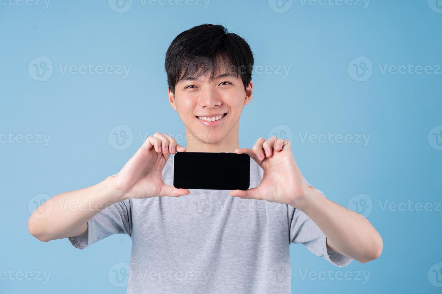 Young Asian man using smartphone on blue background photo