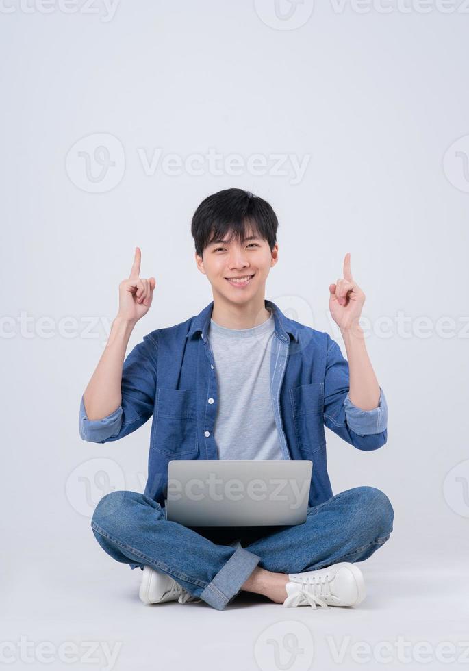 Young Asian man sitting and using laptop on white background photo