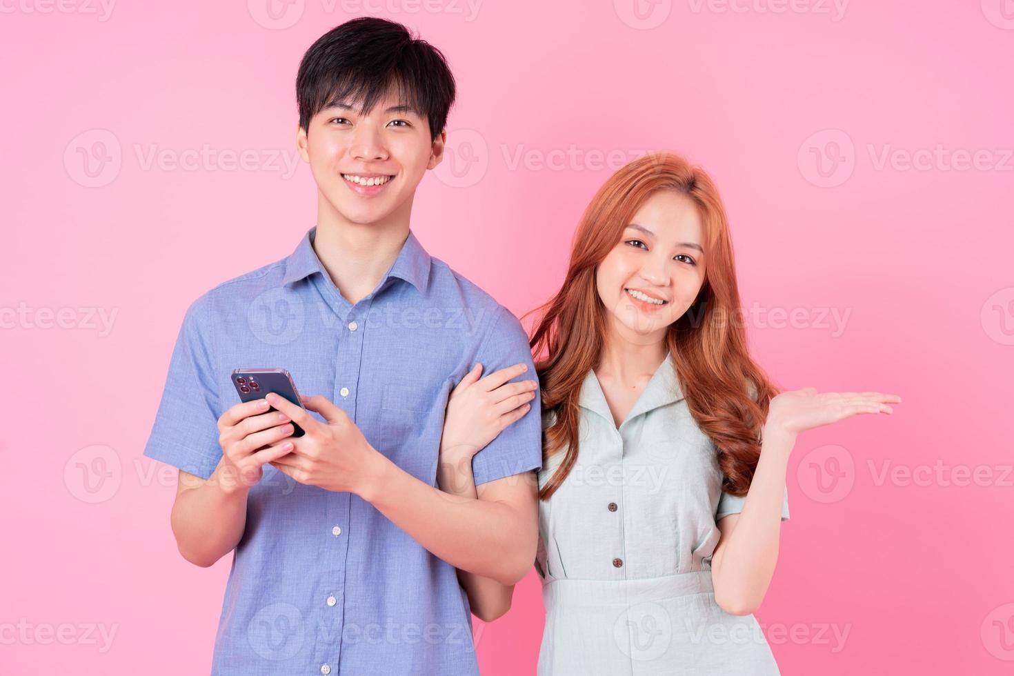 Young Asian couple using smartphone on pink background photo