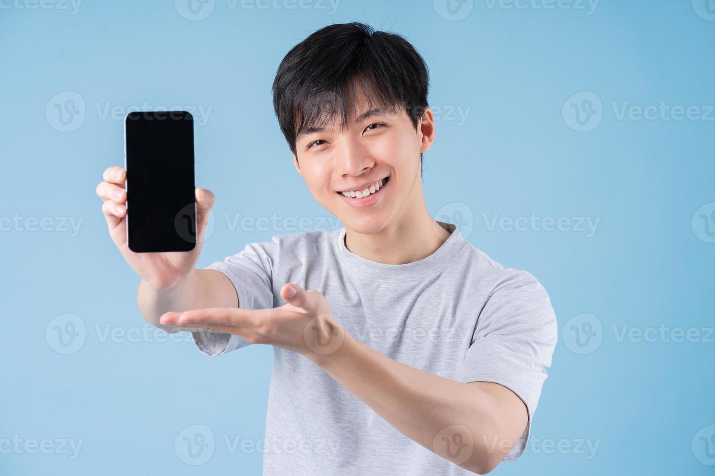 Young Asian man using smartphone on blue background photo