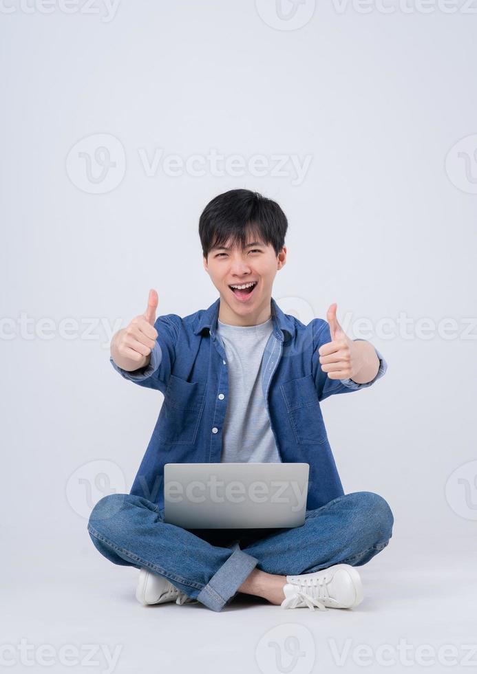 Young Asian man sitting and using laptop on white background photo