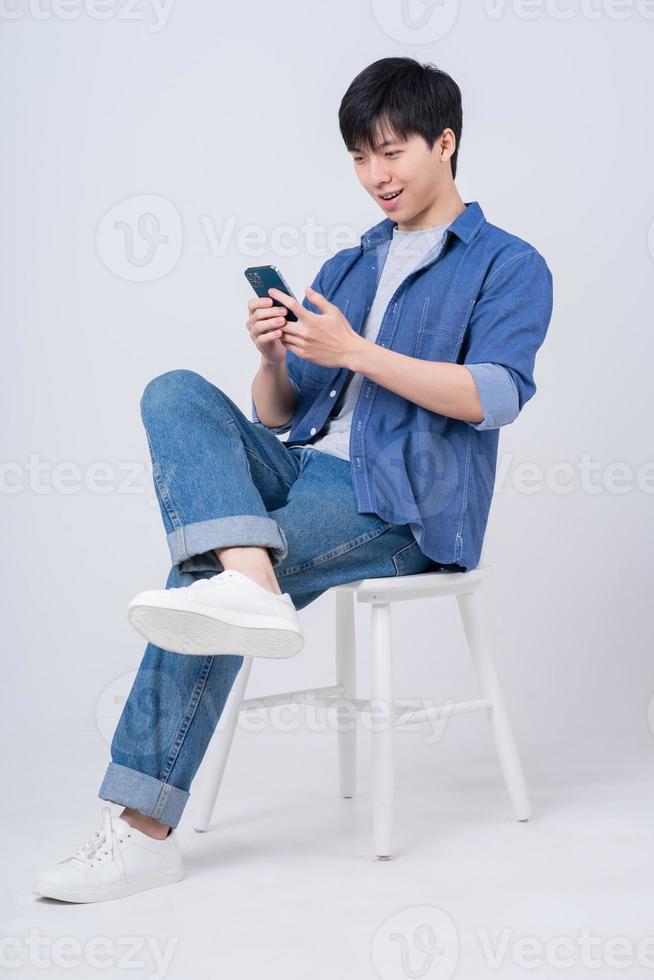 Young Asian man sitting and using smartphone on white background photo