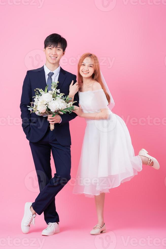 Young Asian bride and groom posing on pink background photo