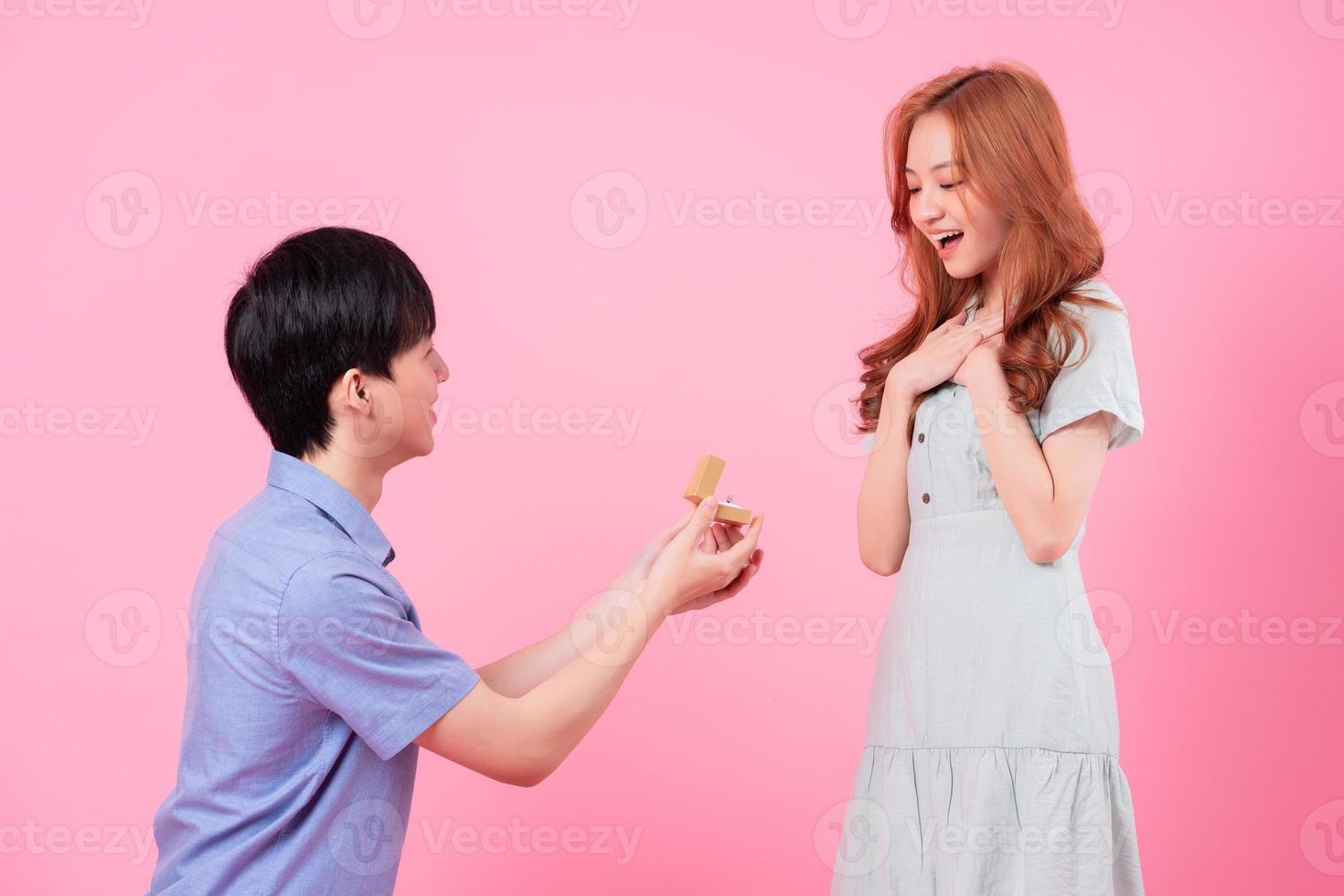 Young Asian man proposes to his girlfriend on a pink background photo