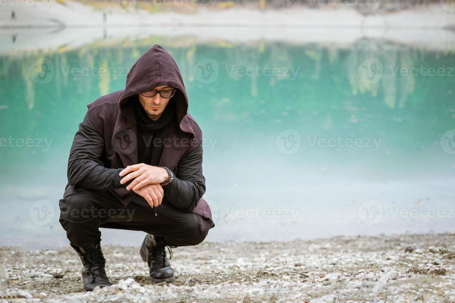 Young man in glasses and vest with a hood on the background of a turquoise lake photo