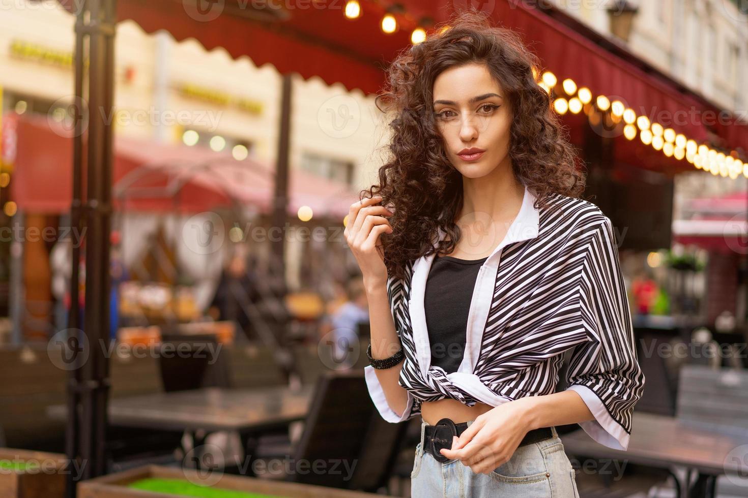 Portrait of a young beautiful woman with curly hair on the street posing for the camera photo