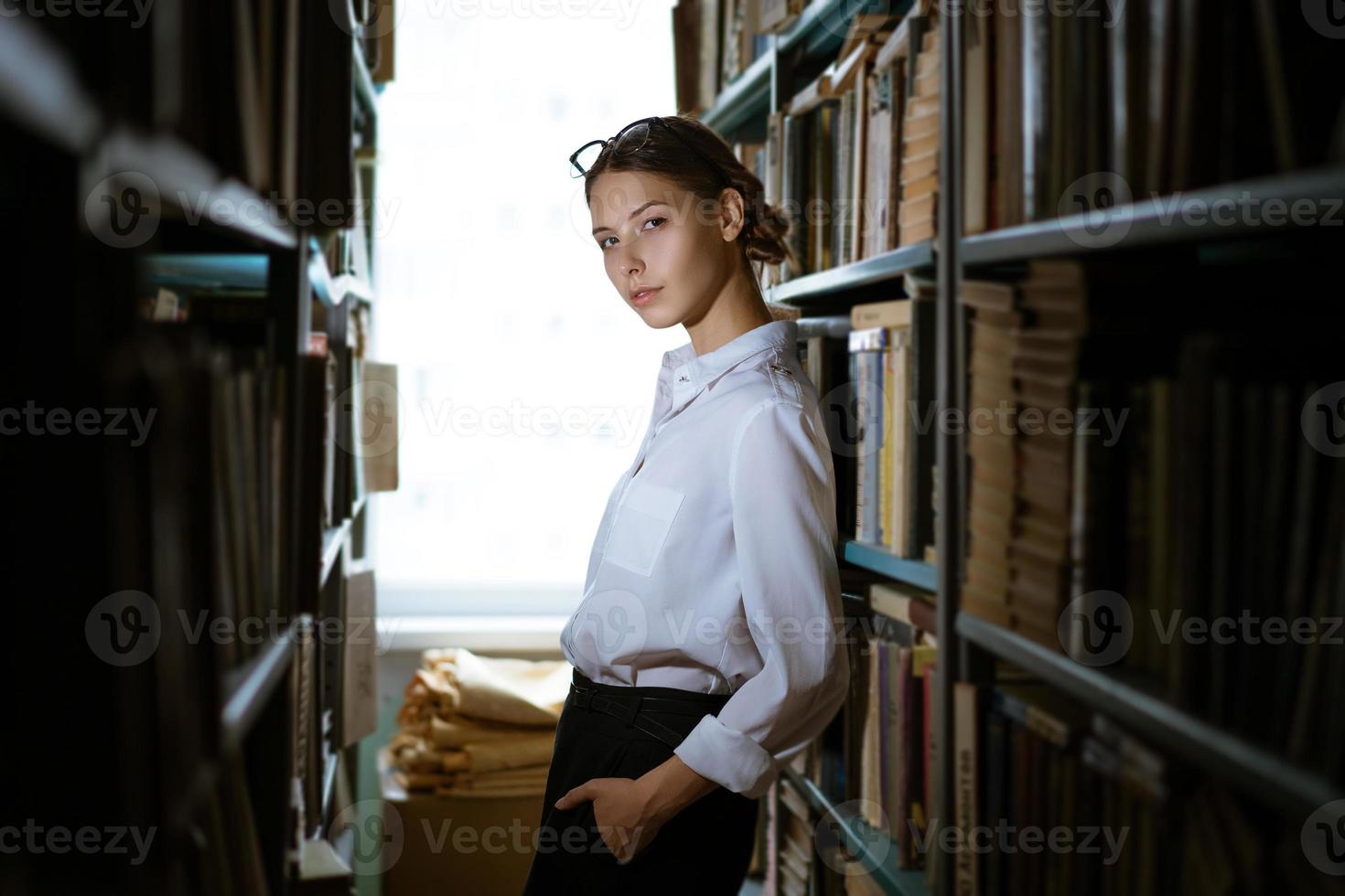 hermosa estudiante se encuentra entre las filas de la biblioteca, foto