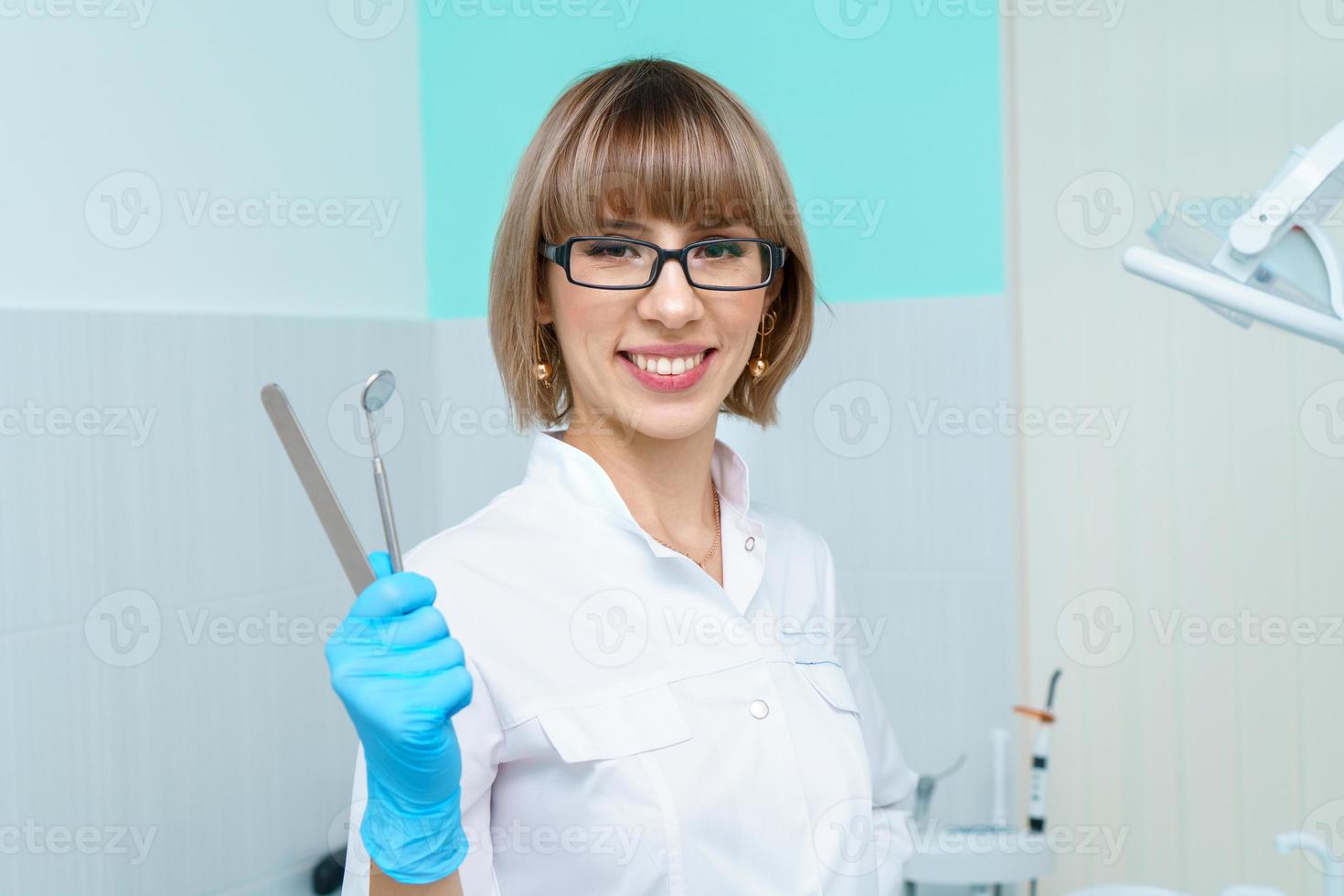 Woman dentist holding tools on background of the dental office in a white coat photo