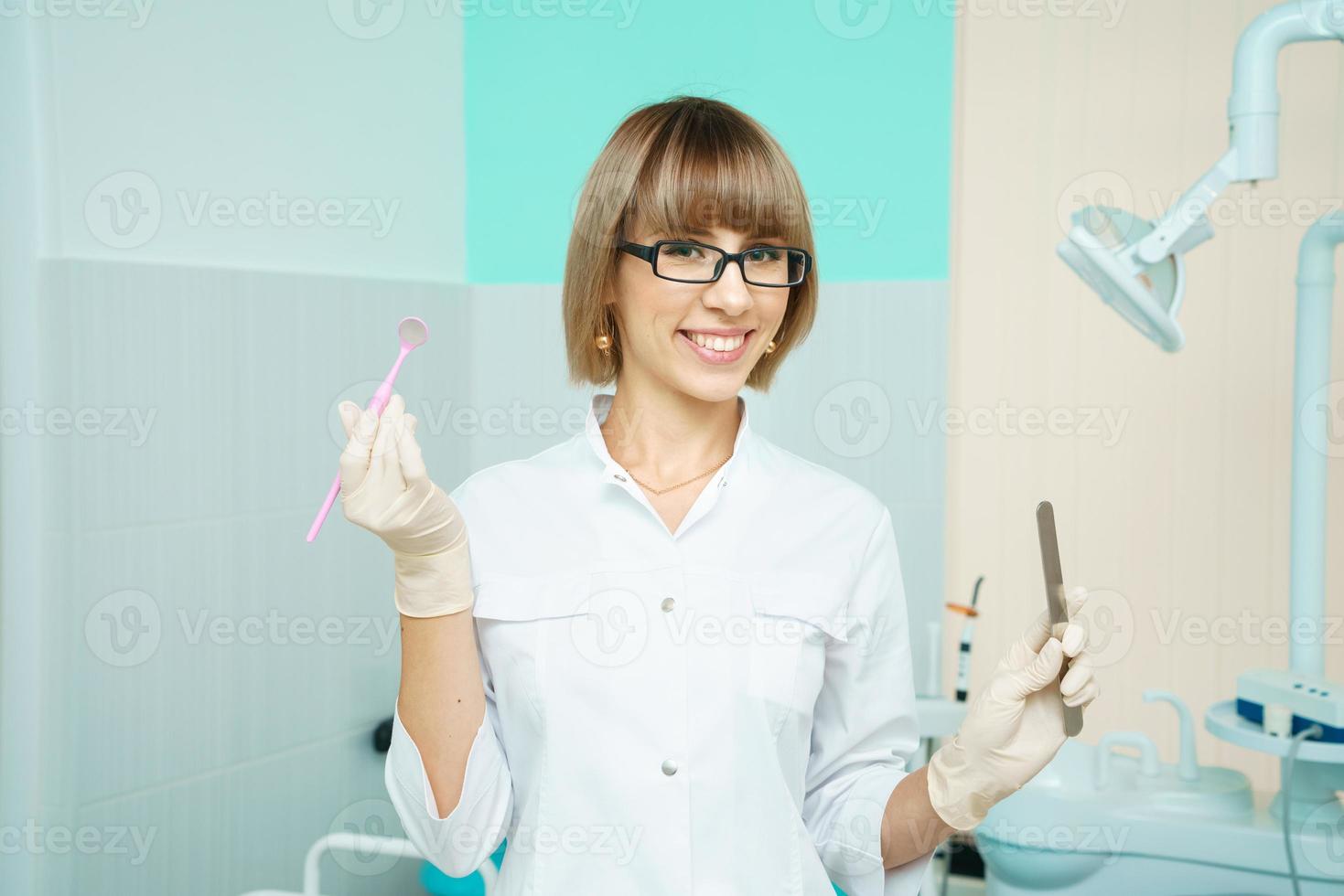 Portrait of happy woman dentist on the background of dental office holding tool photo