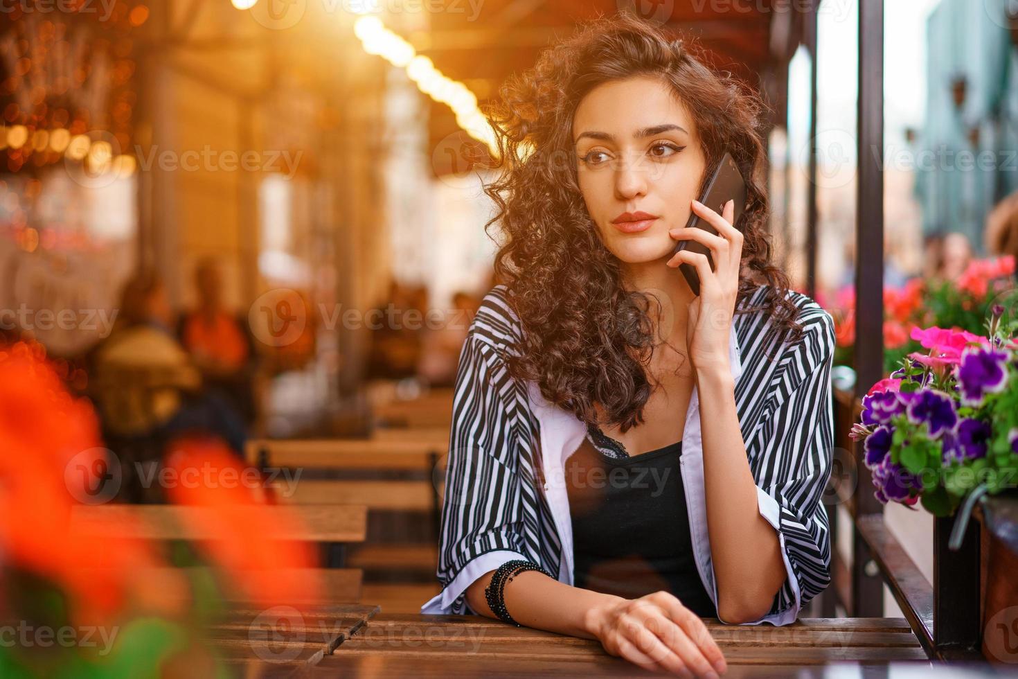 retrato de una mujer joven en un café en la calle sentada en una mesa y hablando por teléfono. concepto de mujer de belleza de estilo de vida. foto