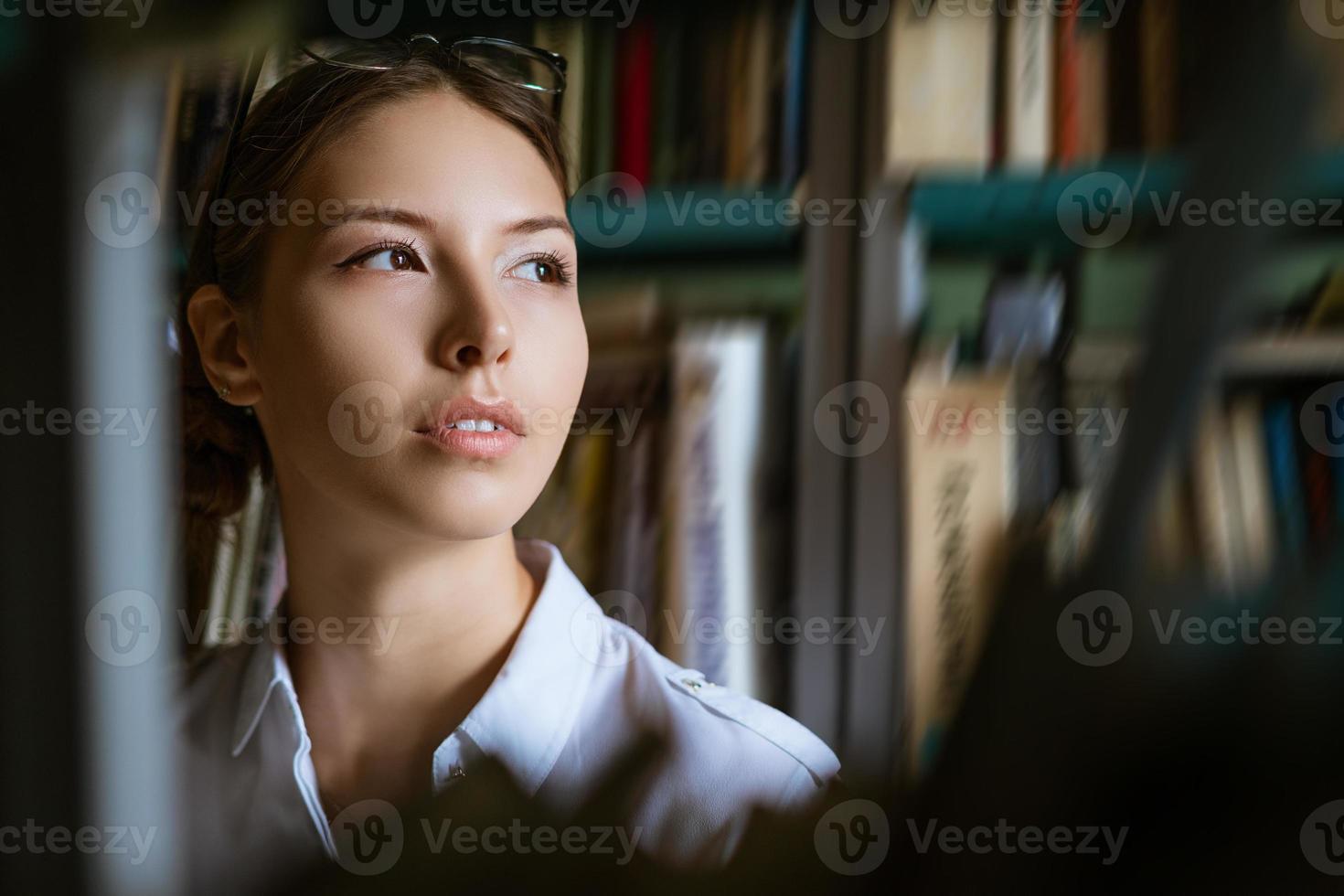 Portrait of a young woman against the background of books in the library photo