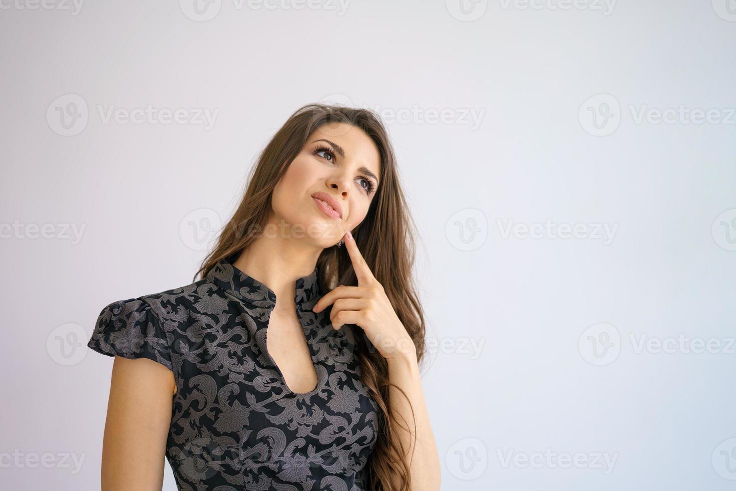 young woman with thoughtful look holds finger to her chin, on white background photo