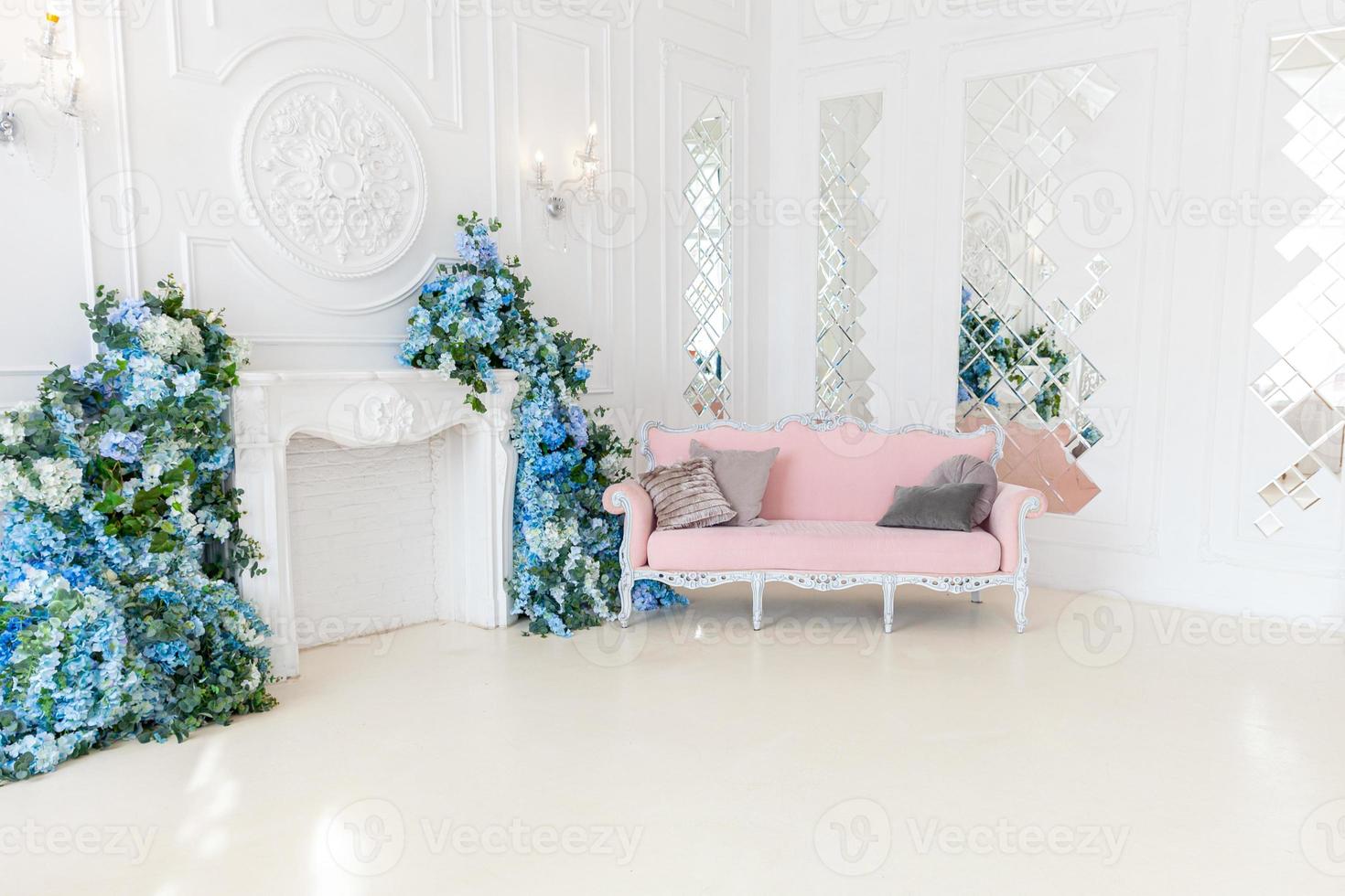 Beautiful luxury classic clean interior living room in white color with pink sofa fireplace flower composition. Bright modern stylish interior living room with furniture in classic minimalist style. photo