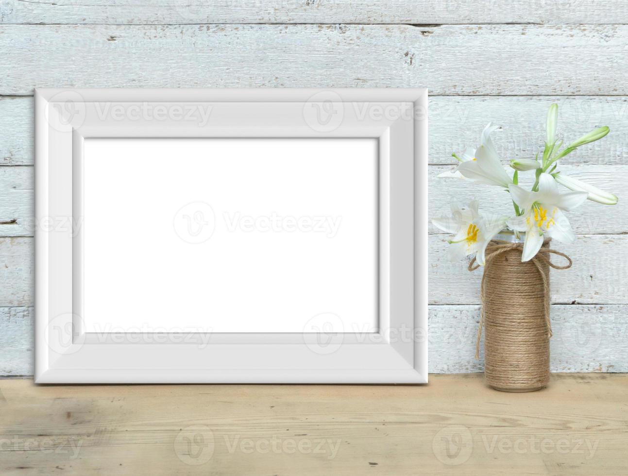 Old horizontal A4 White Wooden Frame mockup near a bouquet of lilies stands on a wooden table on a painted white wooden background. Rustic style, simple beauty. 3d render. photo