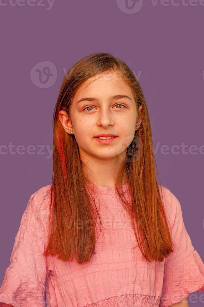 Cute girl with long hair on a purple background in a pink dress. Portrait of a teenagers girl. photo