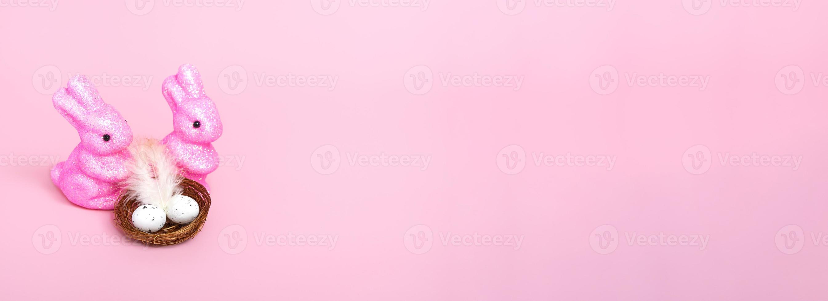Easter bunnies and a nest with eggs on a pink background. Holiday concept. Closeup copy space photo