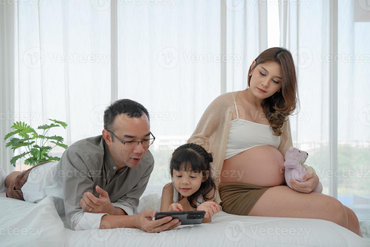 padre y madre viendo dibujos animados desde un teléfono inteligente con una hija pequeña en el dormitorio foto