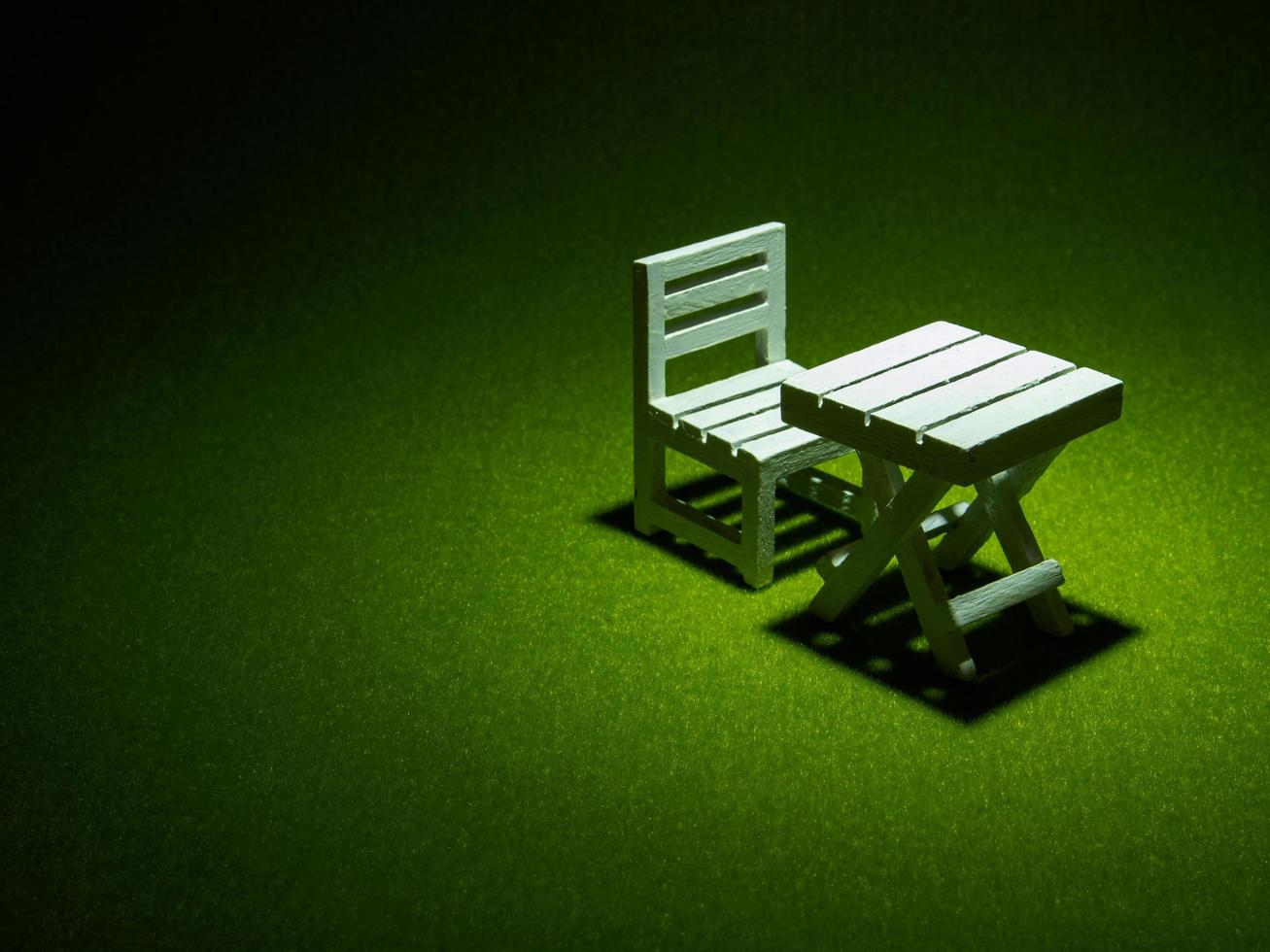 White wooden chair and table on artificial grass. Light shining down from above In the drak tone photo