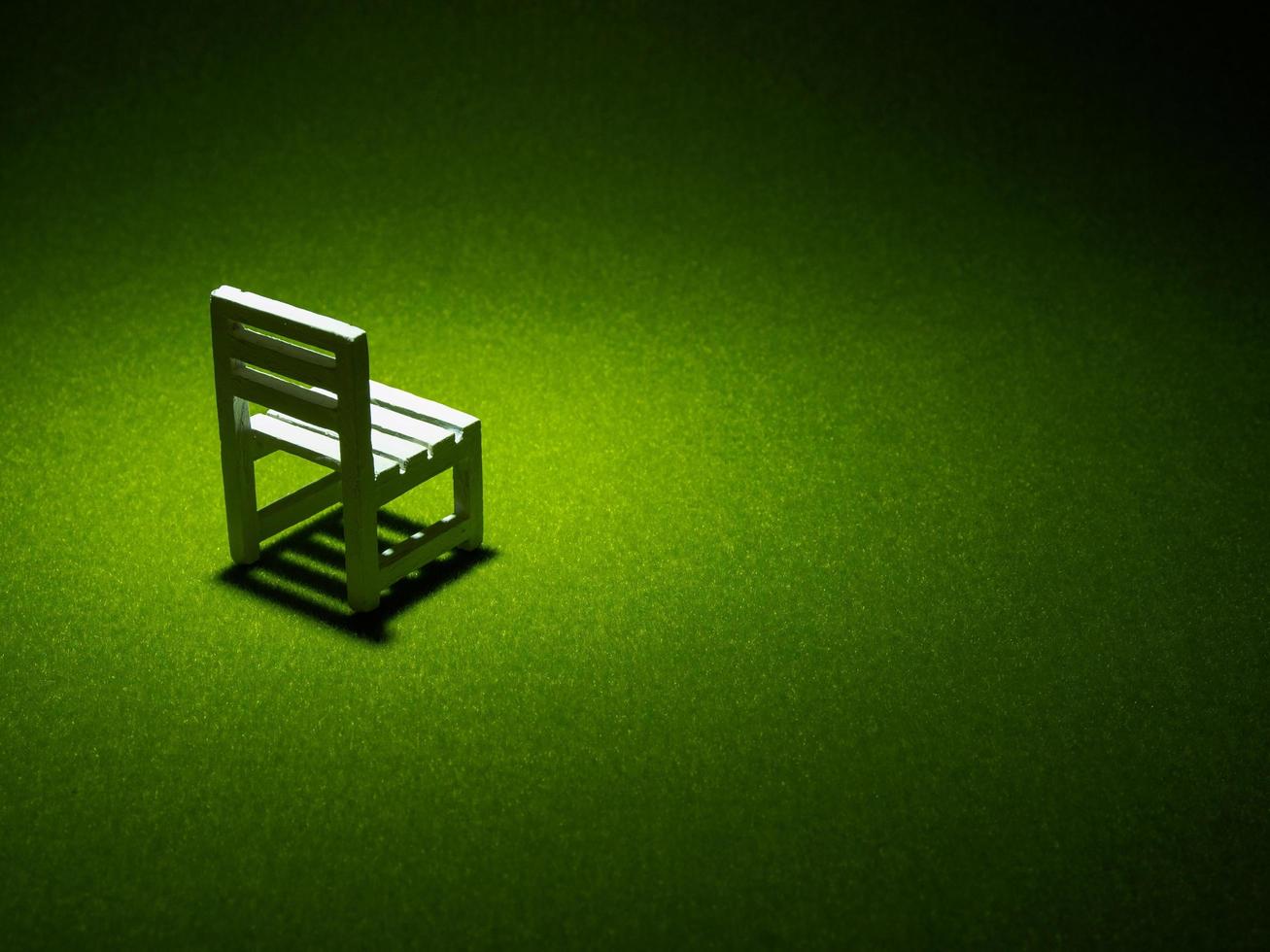 White wooden chair on artificial grass. Light shining down from above in the dark tone low key photo