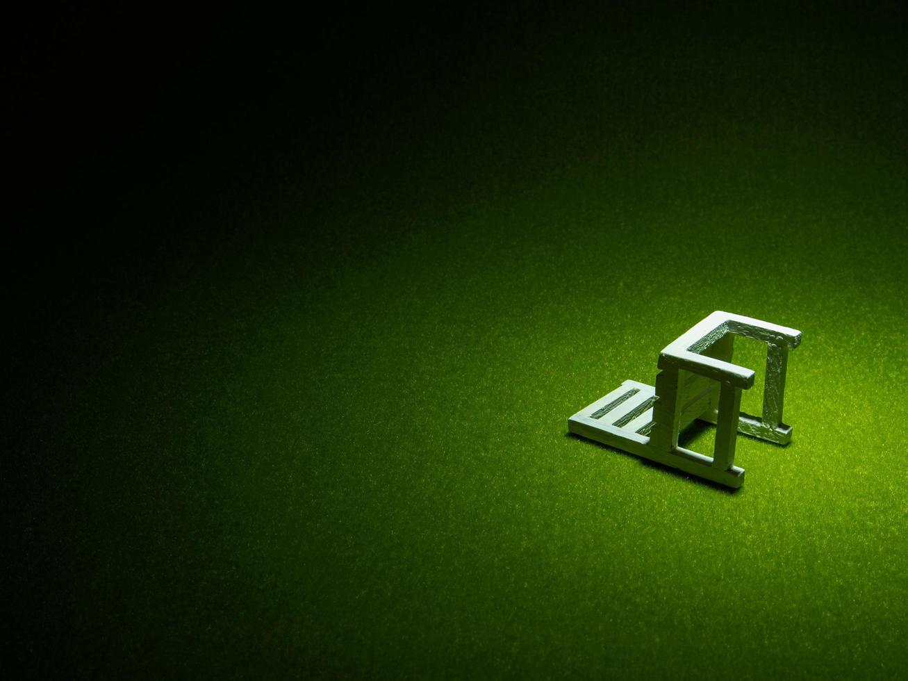 White wooden chair on artificial grass. Light shining down from above in the dark tone low key photo